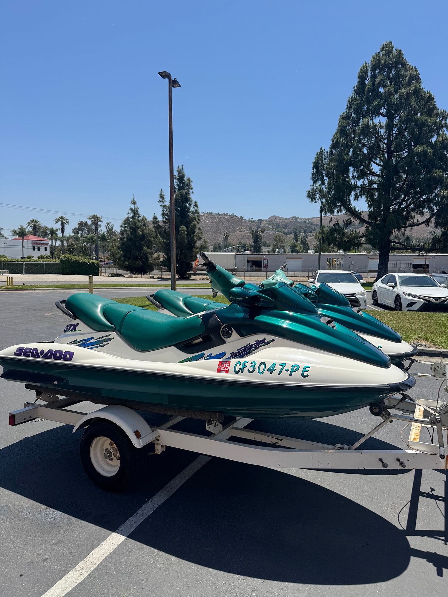 Two green jet skis on a trailer in a parking lot on a sunny day.