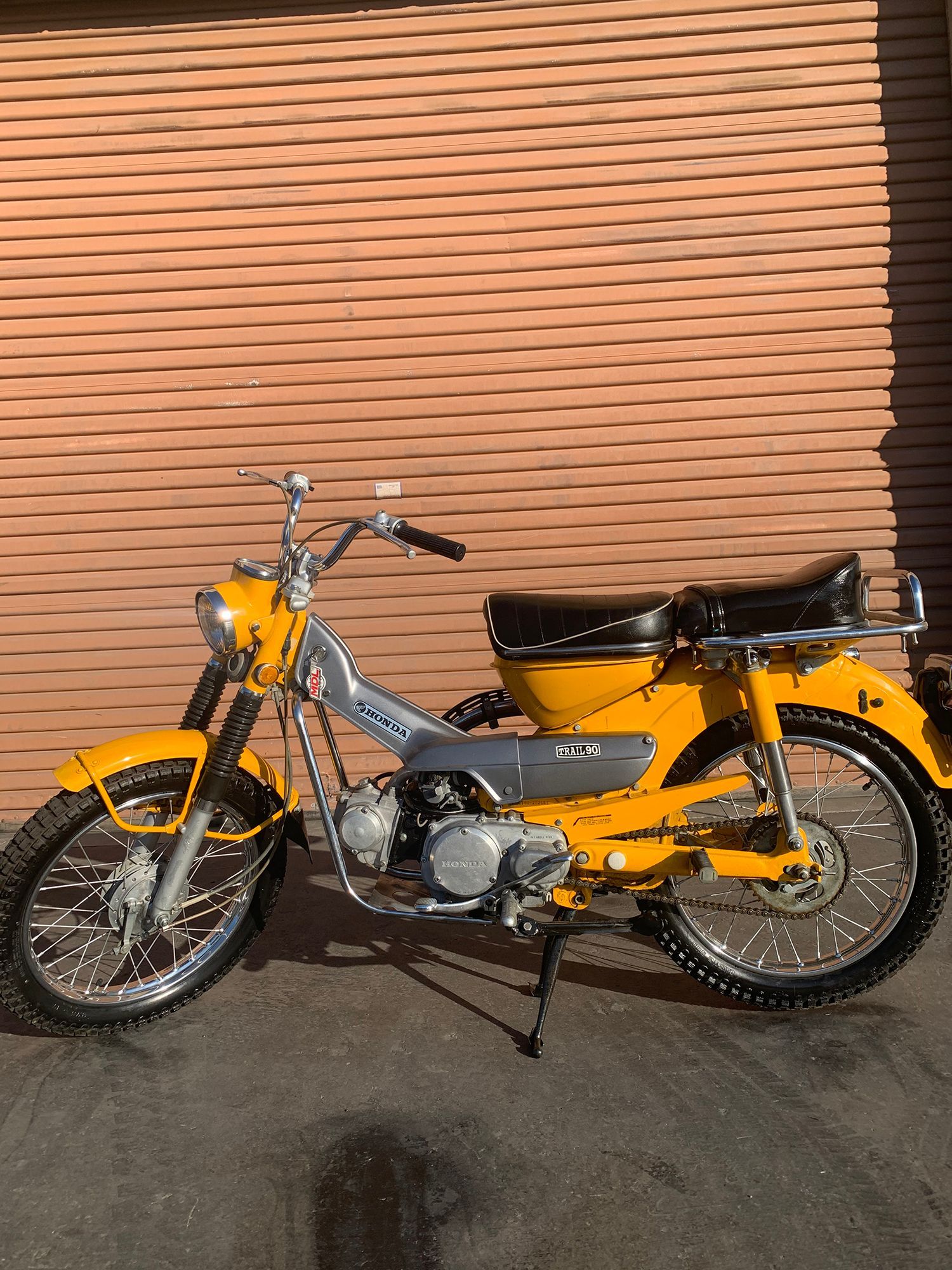 Yellow vintage Honda Super Cub motorcycle parked in front of a brick wall.