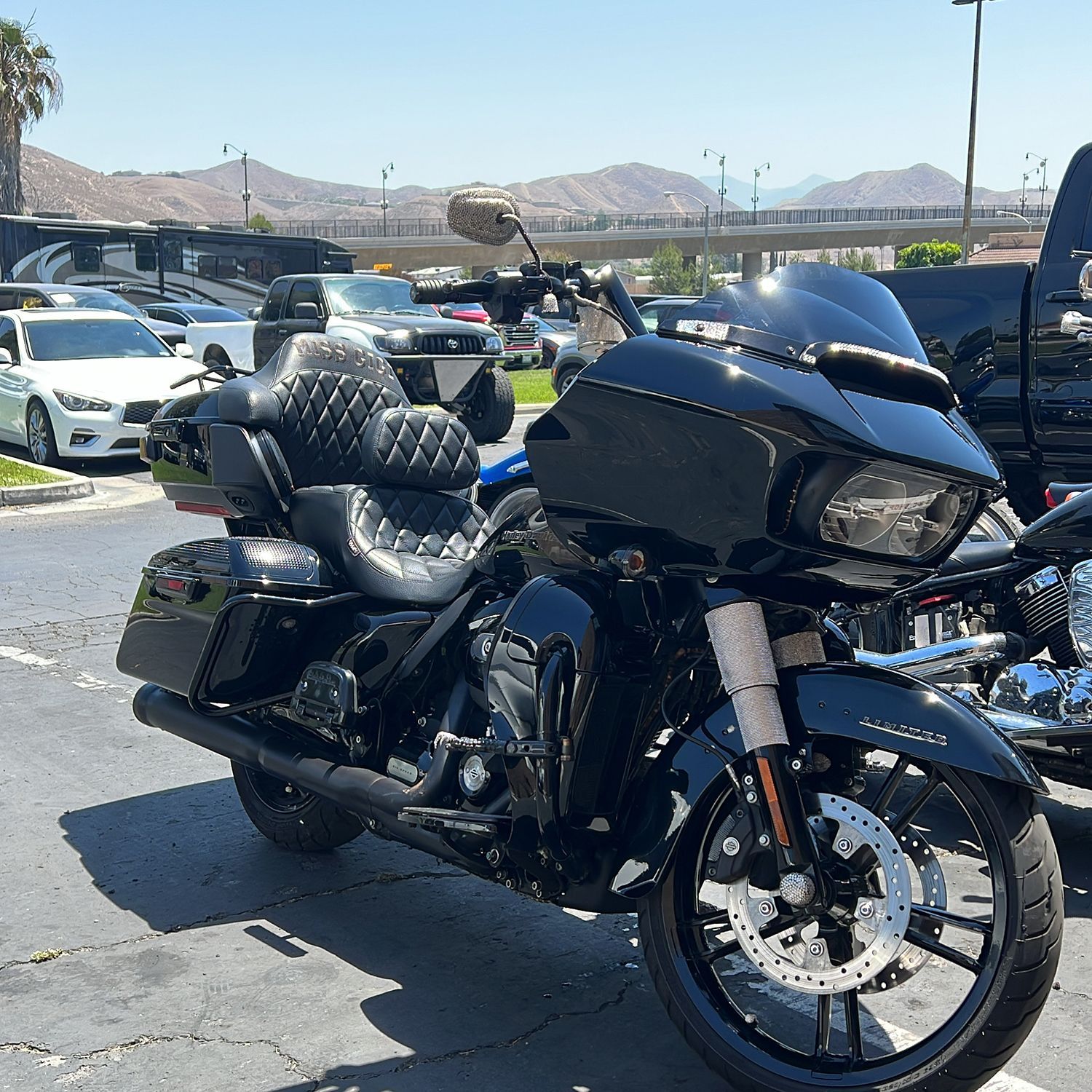 Black Harley-Davidson motorcycle parked outdoors on a sunny day, with mountains and vehicles in the background.