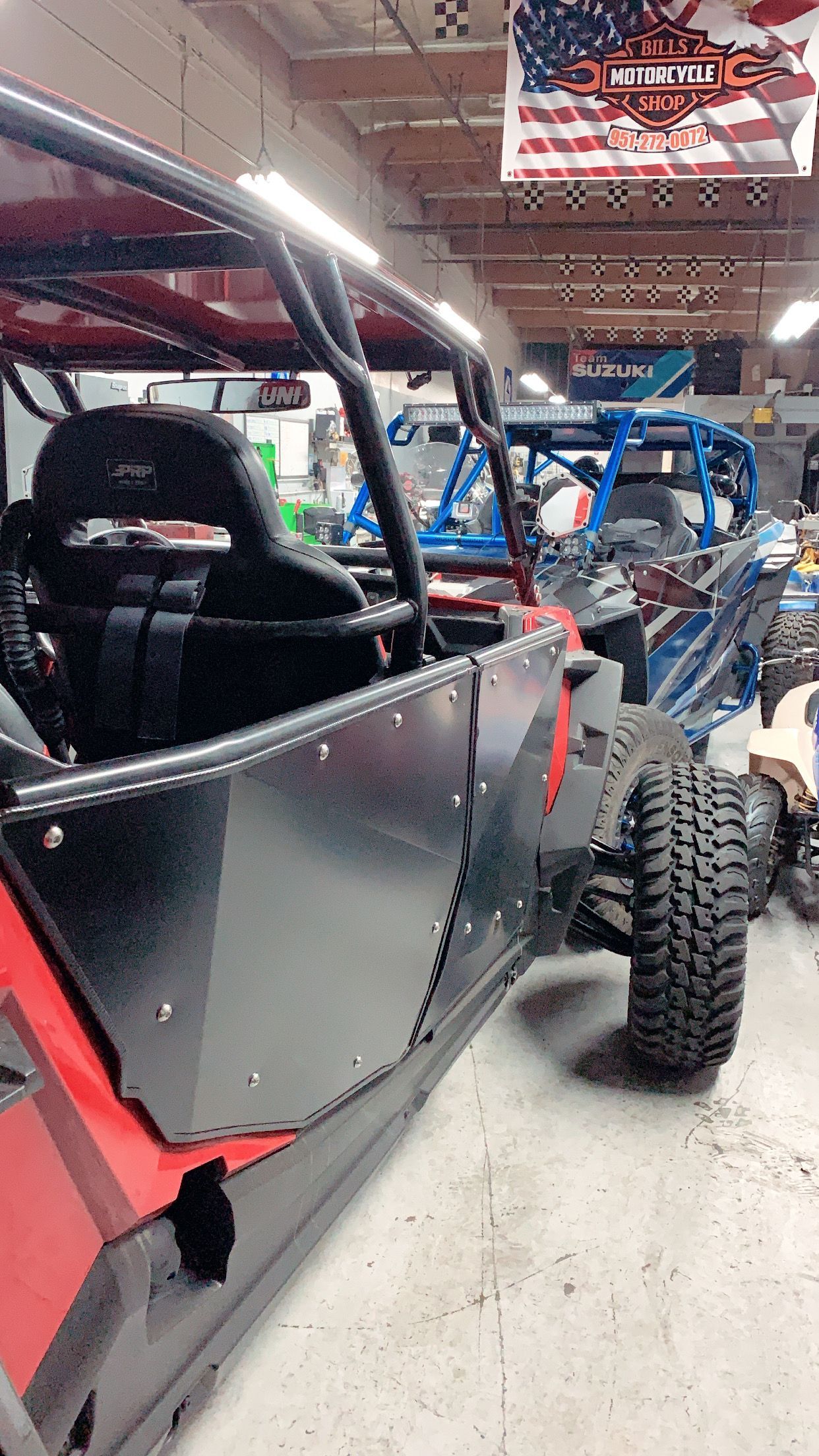 Side-view of a red and black off-road vehicle with a roll cage, inside a garage.