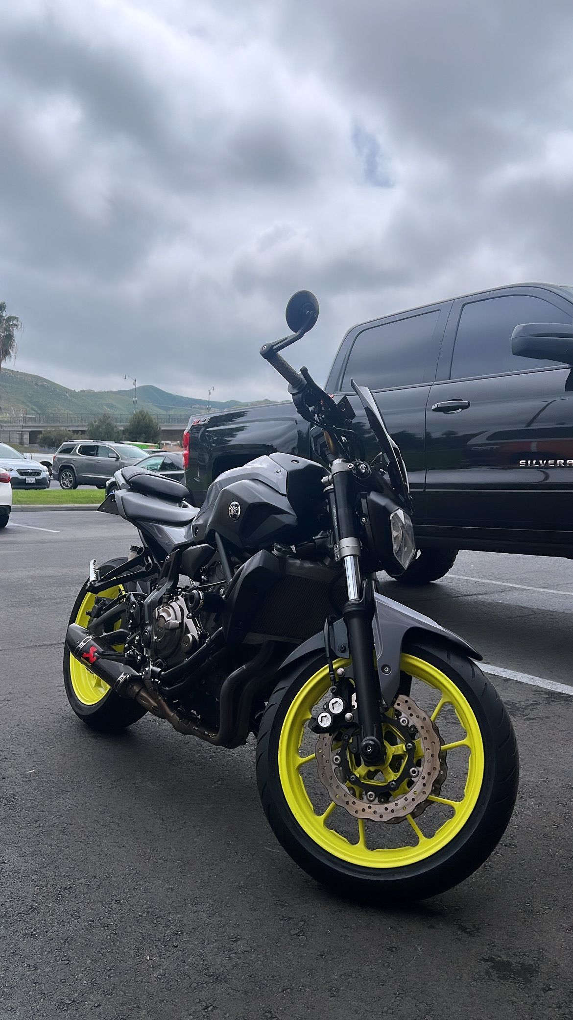 Black Yamaha motorcycle with neon yellow wheels parked on asphalt under a cloudy sky.