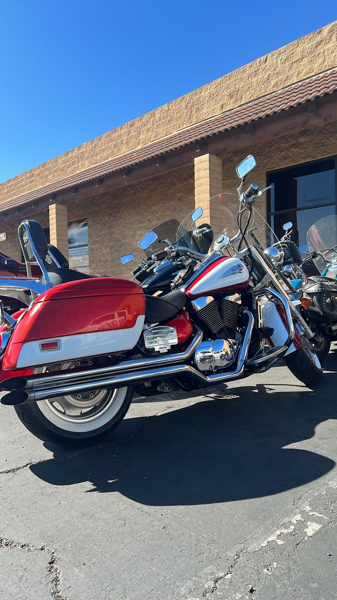 Red and white motorcycle parked in front of a brick building on a sunny day.
