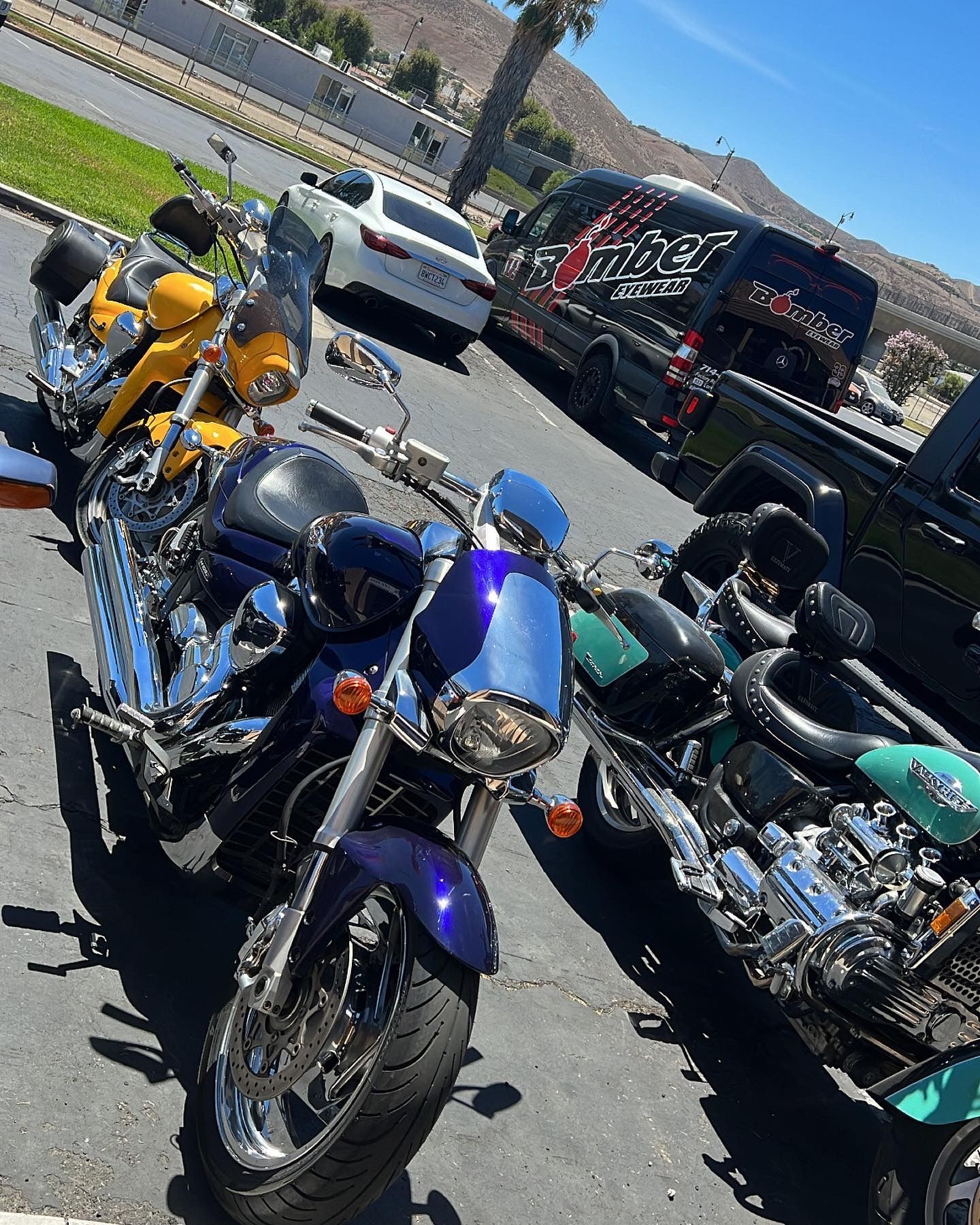 Motorcycles parked in a lot: blue, yellow, and green cruisers under a sunny sky.