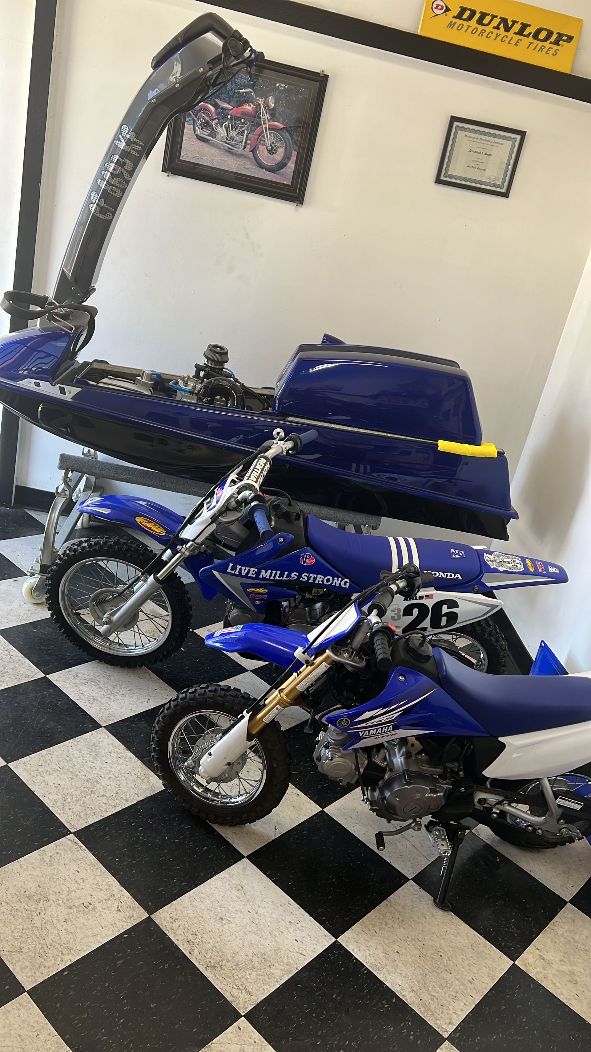Three Yamaha motorcycles and a jetski inside, black and white checkered floor. Blue and white color scheme.