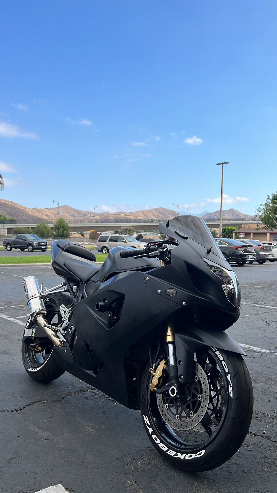 Black sport motorcycle parked on asphalt with a mountain background and clear blue sky.