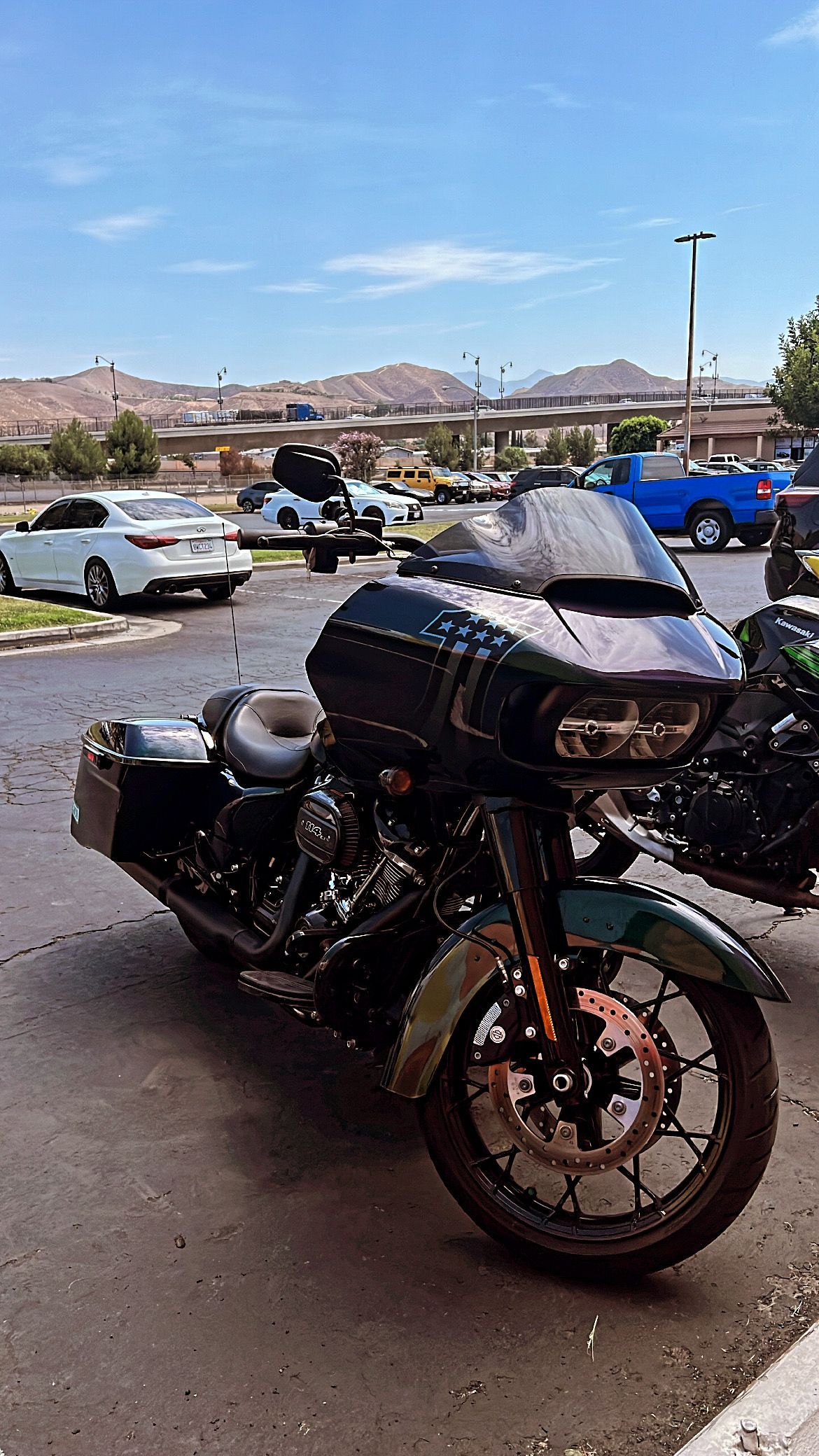 Dark green motorcycle parked outdoors. Buildings and blue sky in the background.