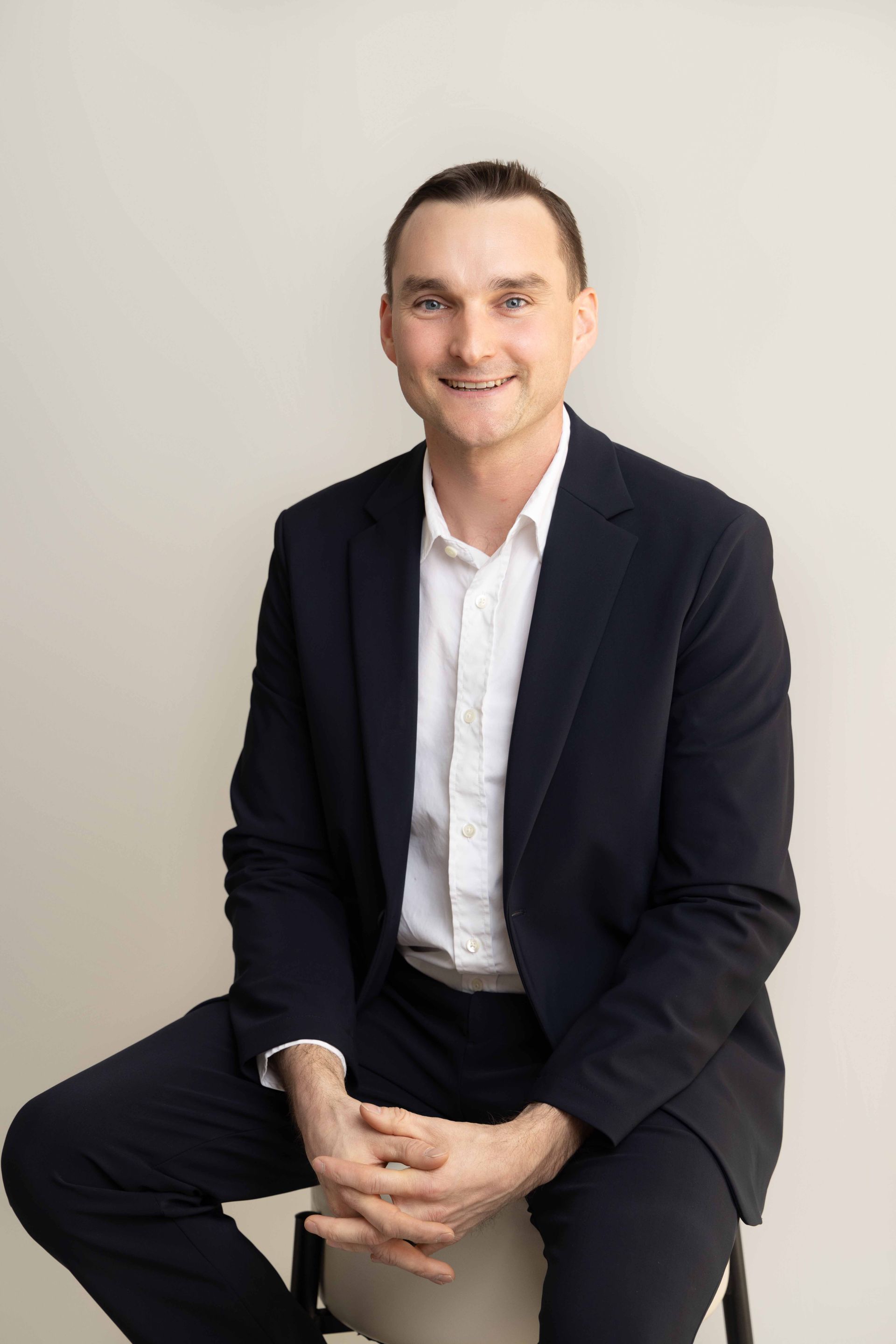 A man in a suit and white shirt is sitting on a chair.