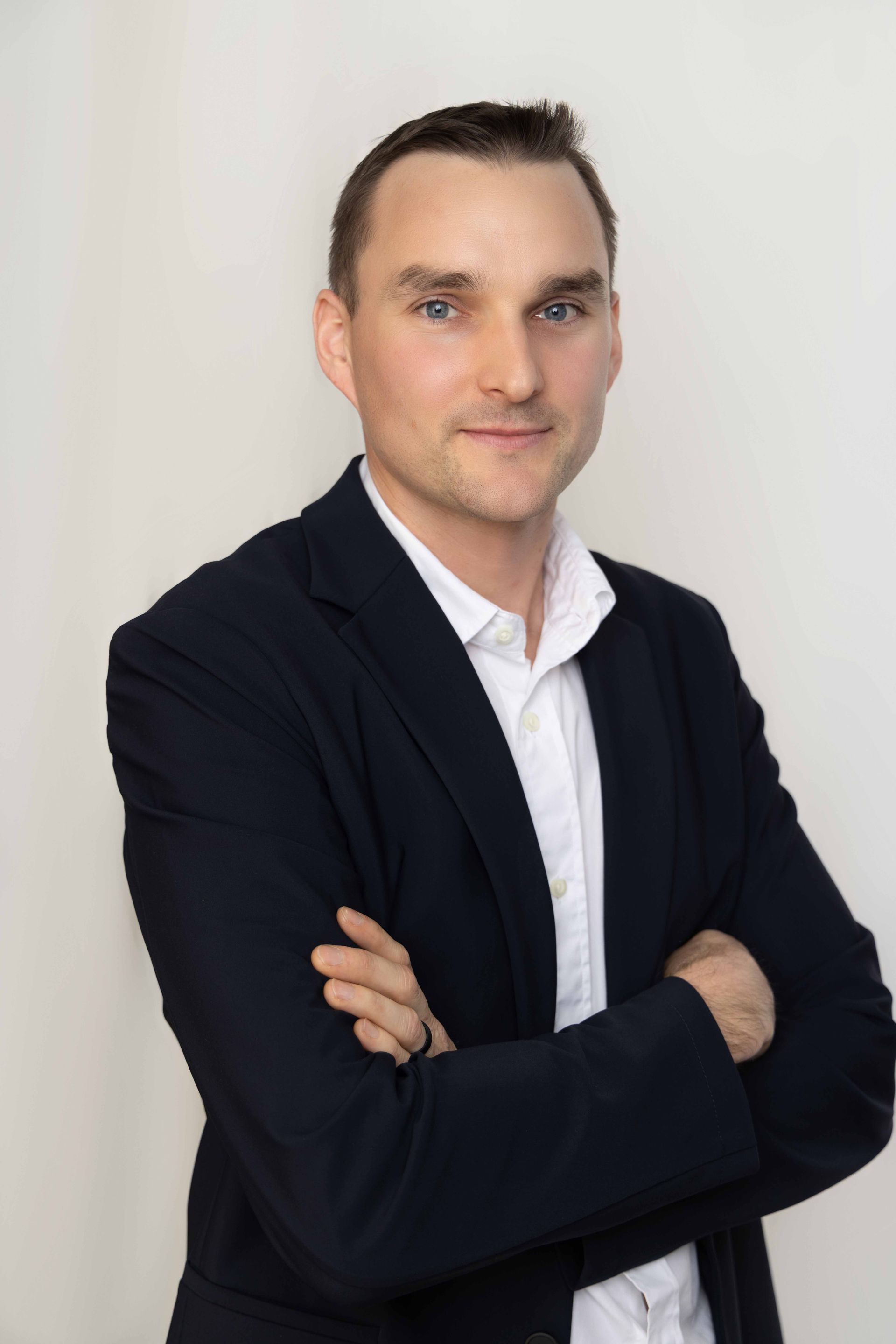 A man in a suit and white shirt is standing with his arms crossed.