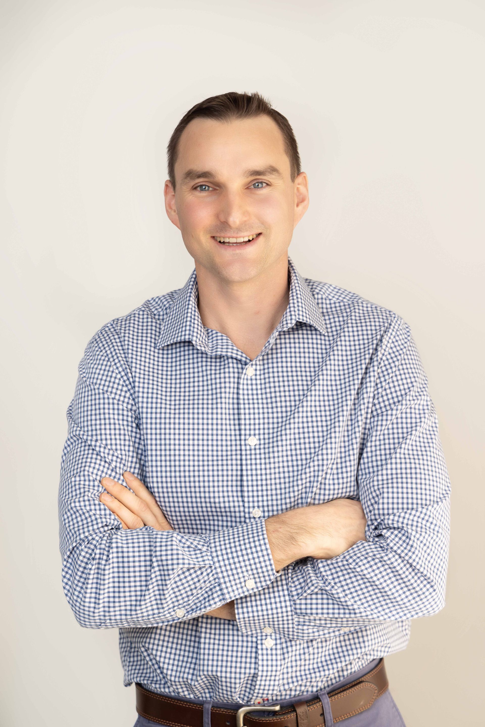A man in a plaid shirt is standing with his arms crossed and smiling.