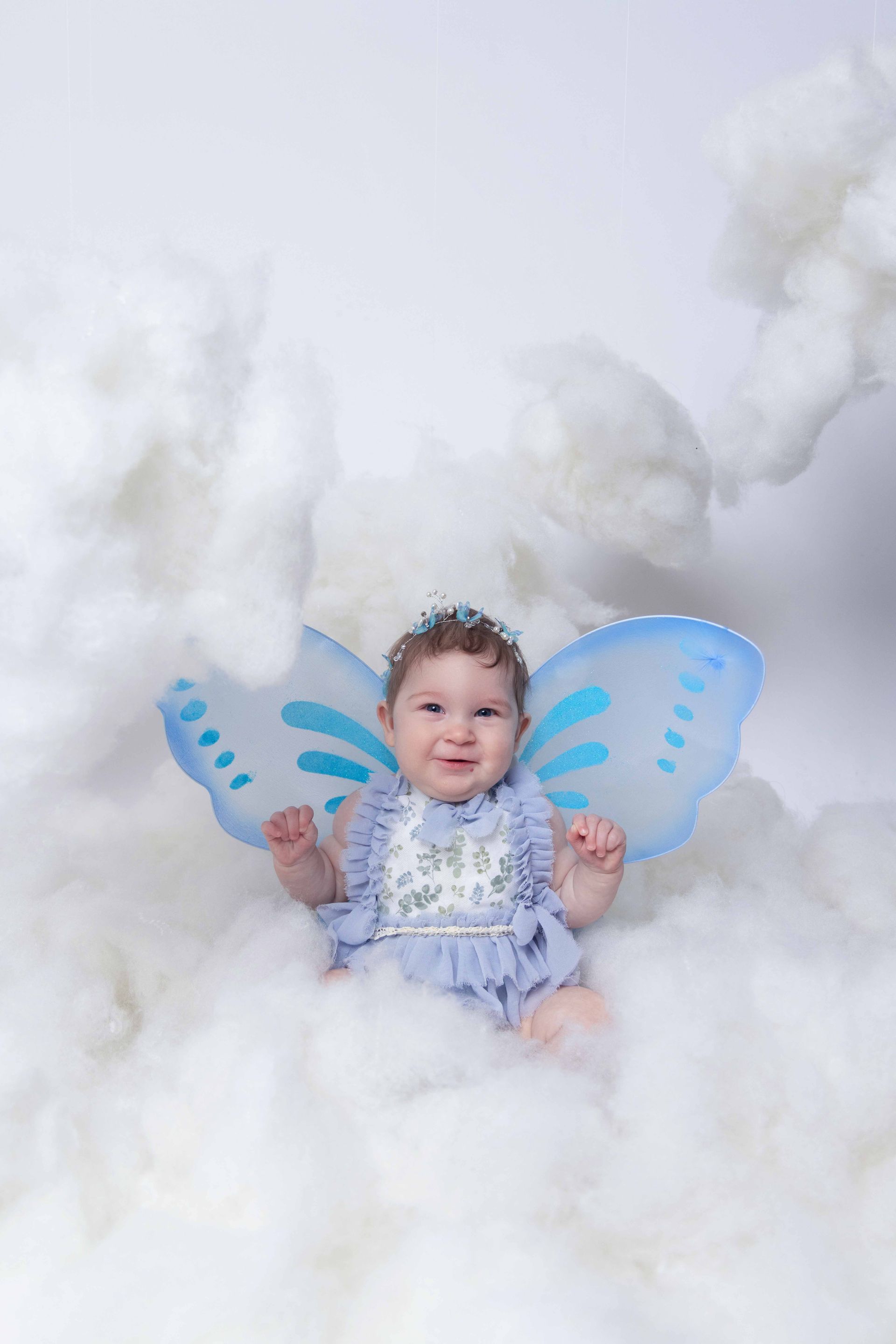 A baby girl wearing fairy wings is sitting in the clouds.