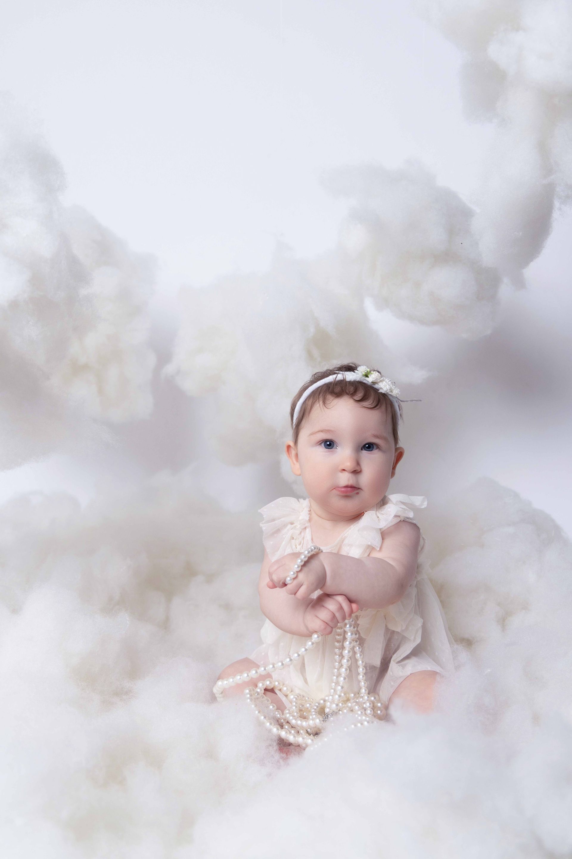 A baby girl is sitting in a pile of white clouds.