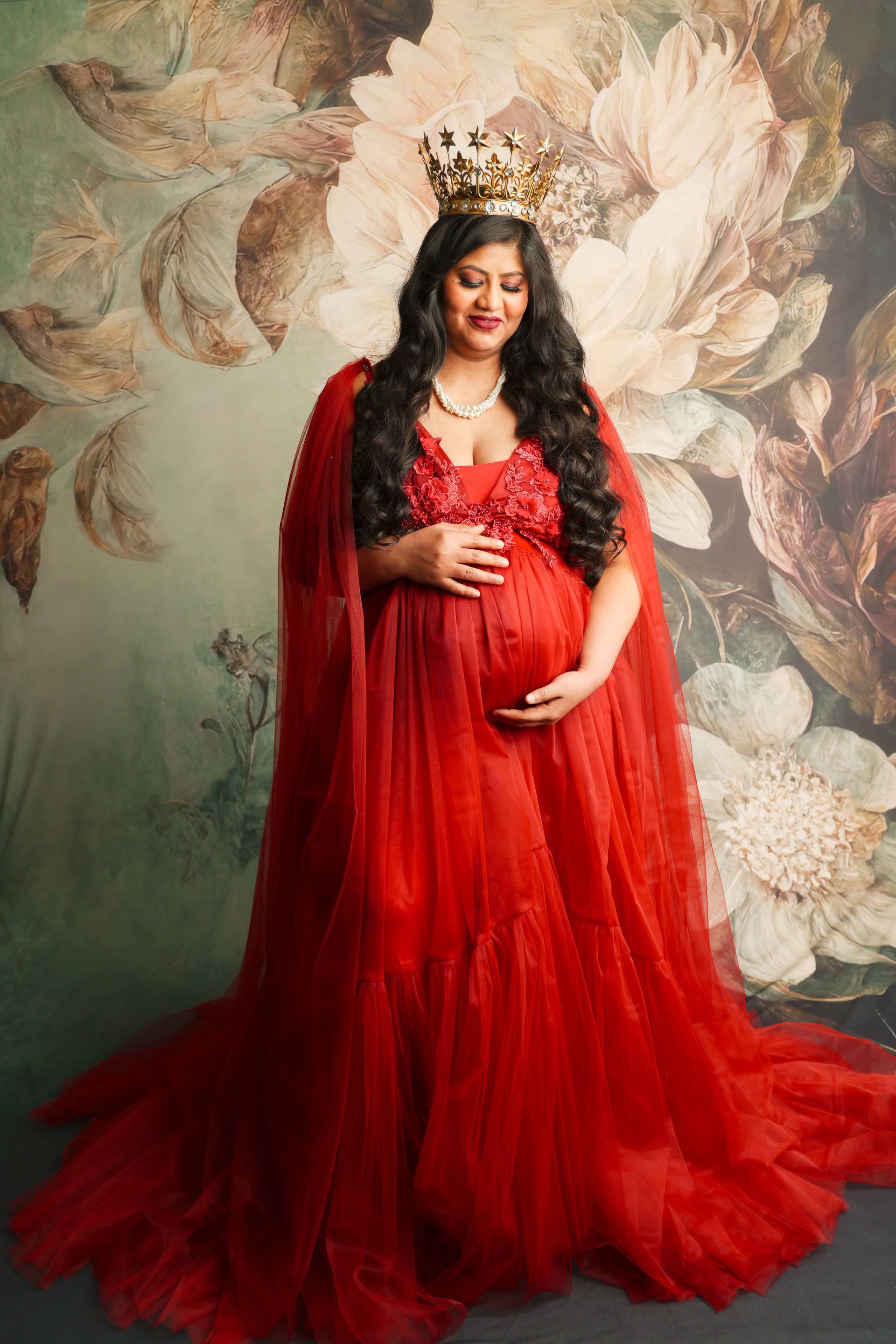 A pregnant woman is wearing a red dress and a crown.