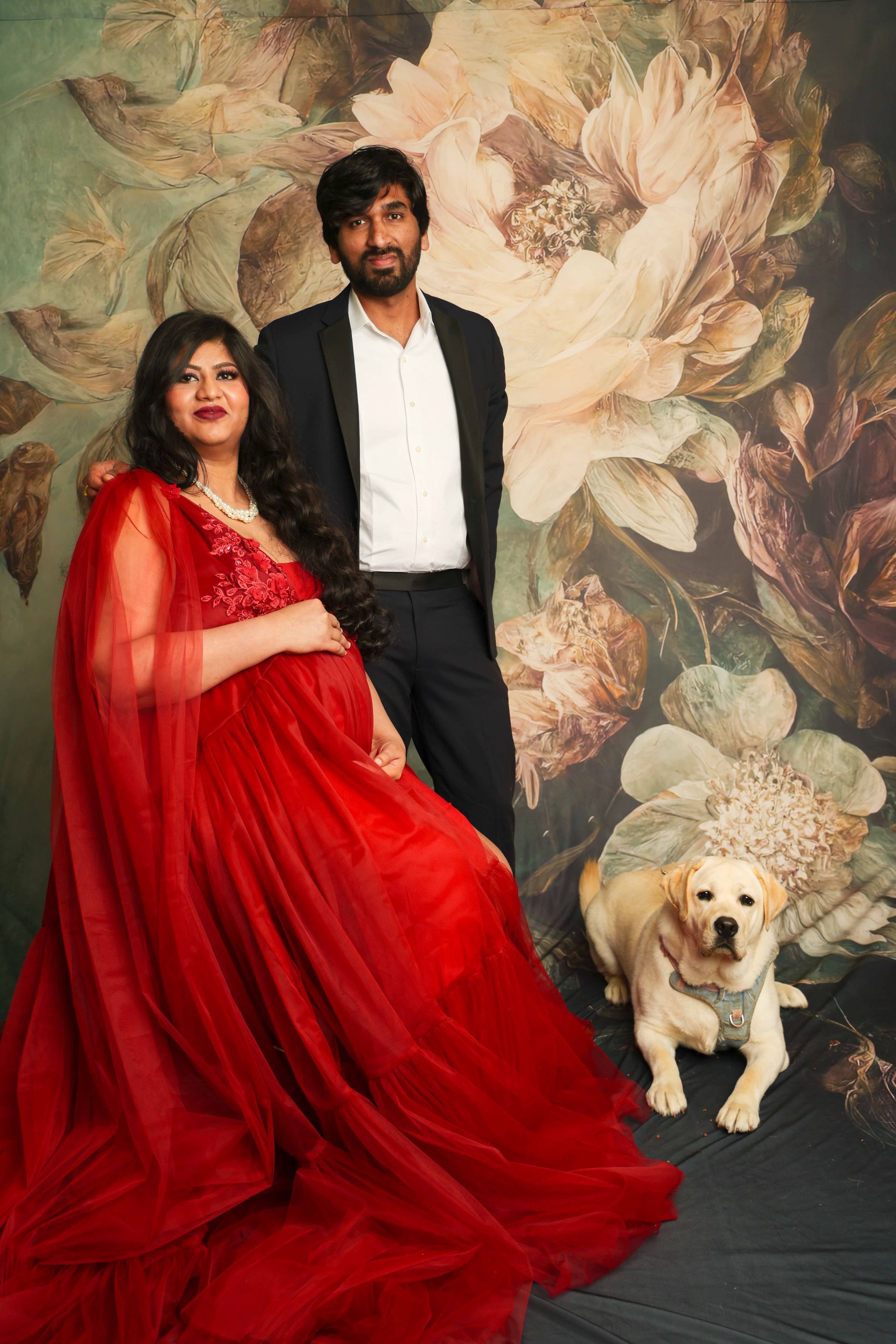 A pregnant woman in a red dress is standing next to a man and a dog.
