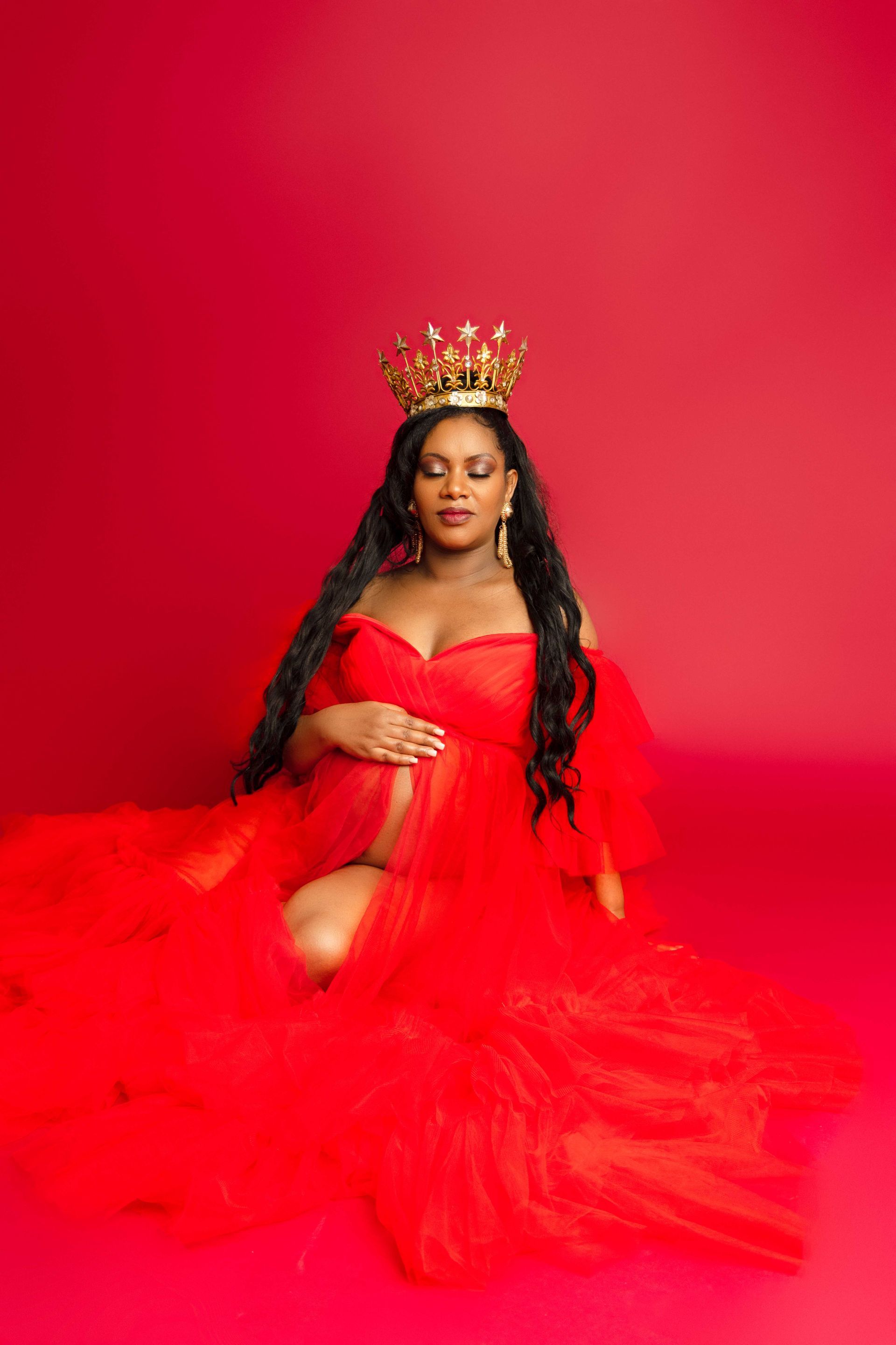 A pregnant woman is wearing a red dress and a crown.