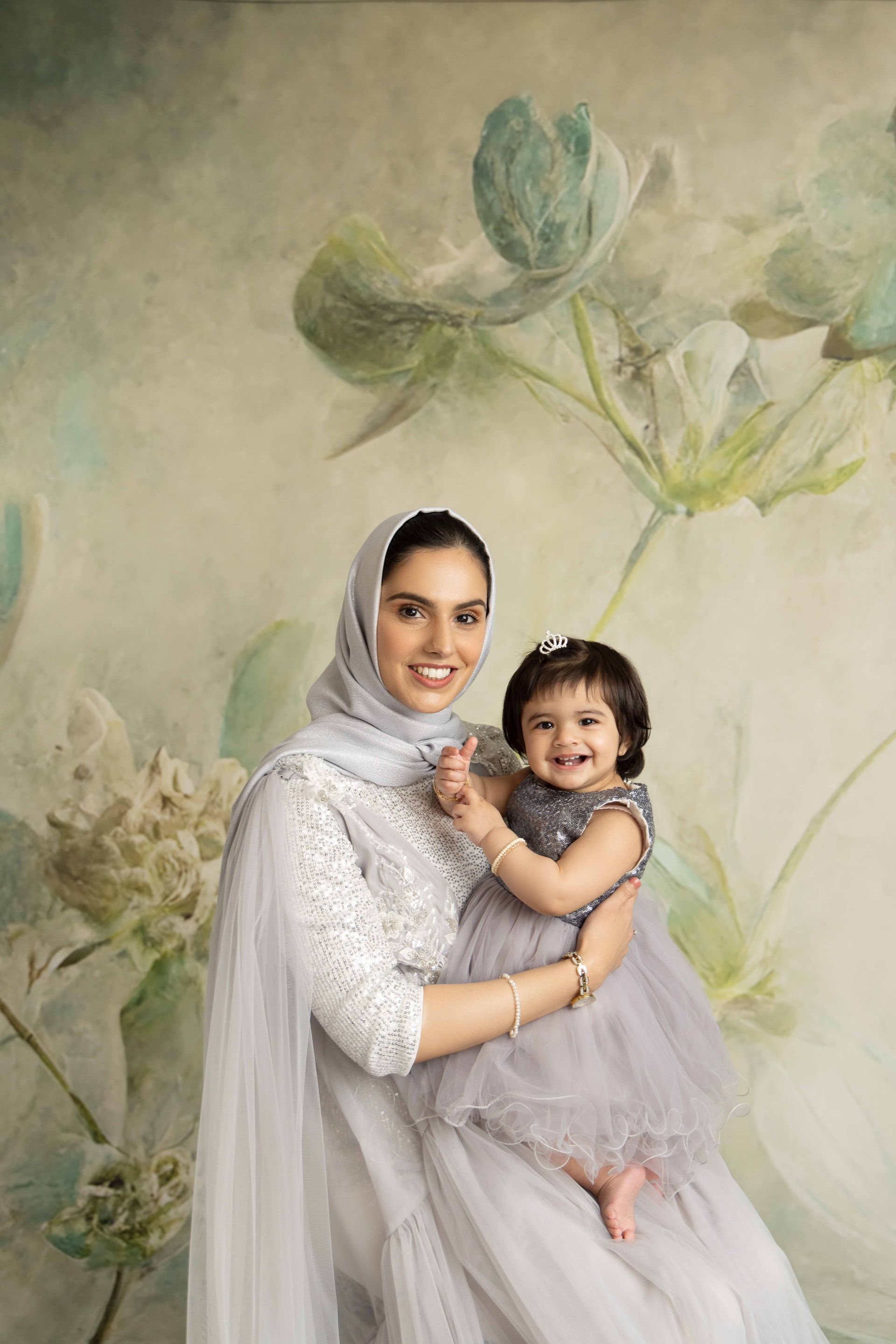 A woman is holding a little girl in her arms in front of a floral background.