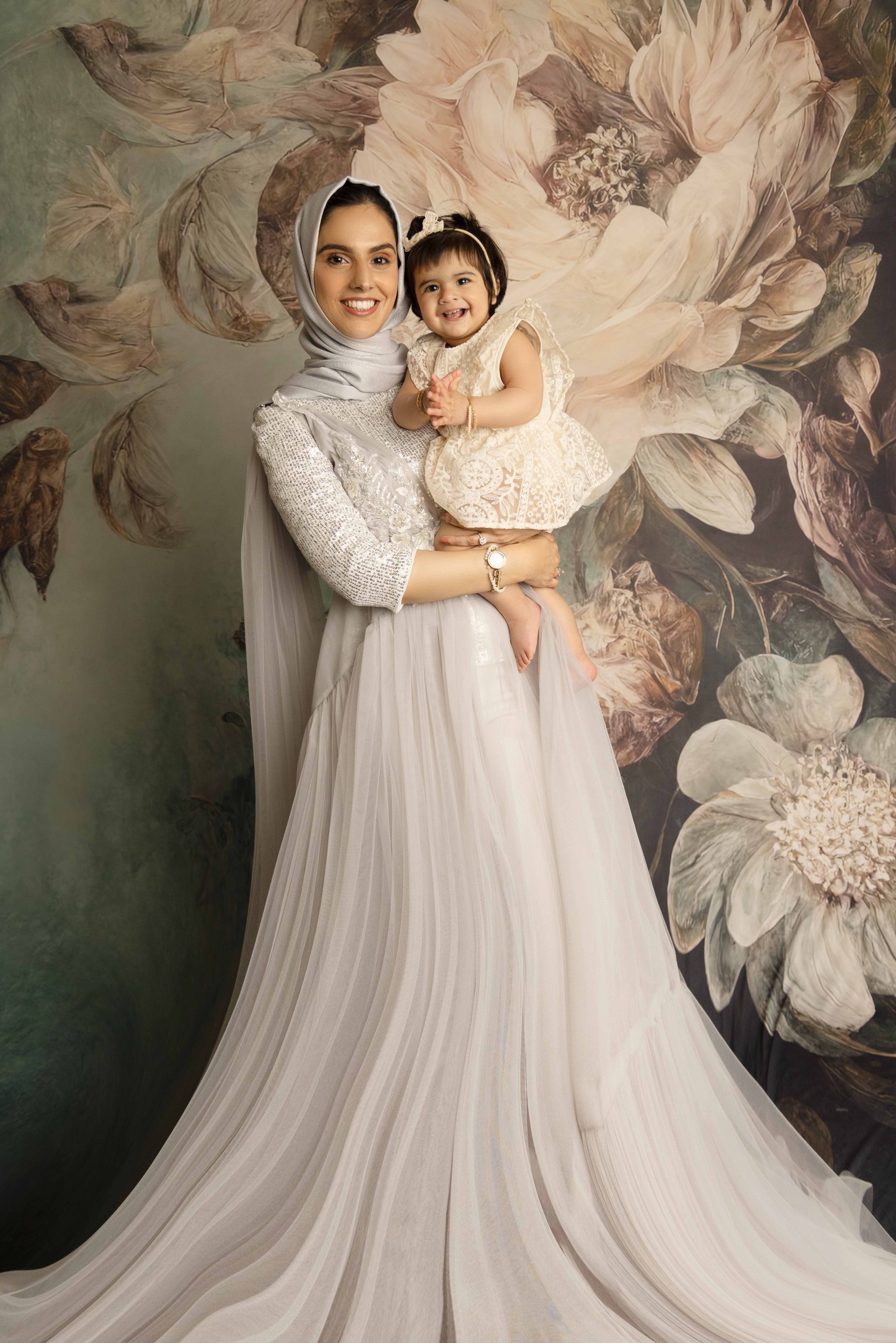 A man is holding a baby girl in his arms in front of a floral wall.