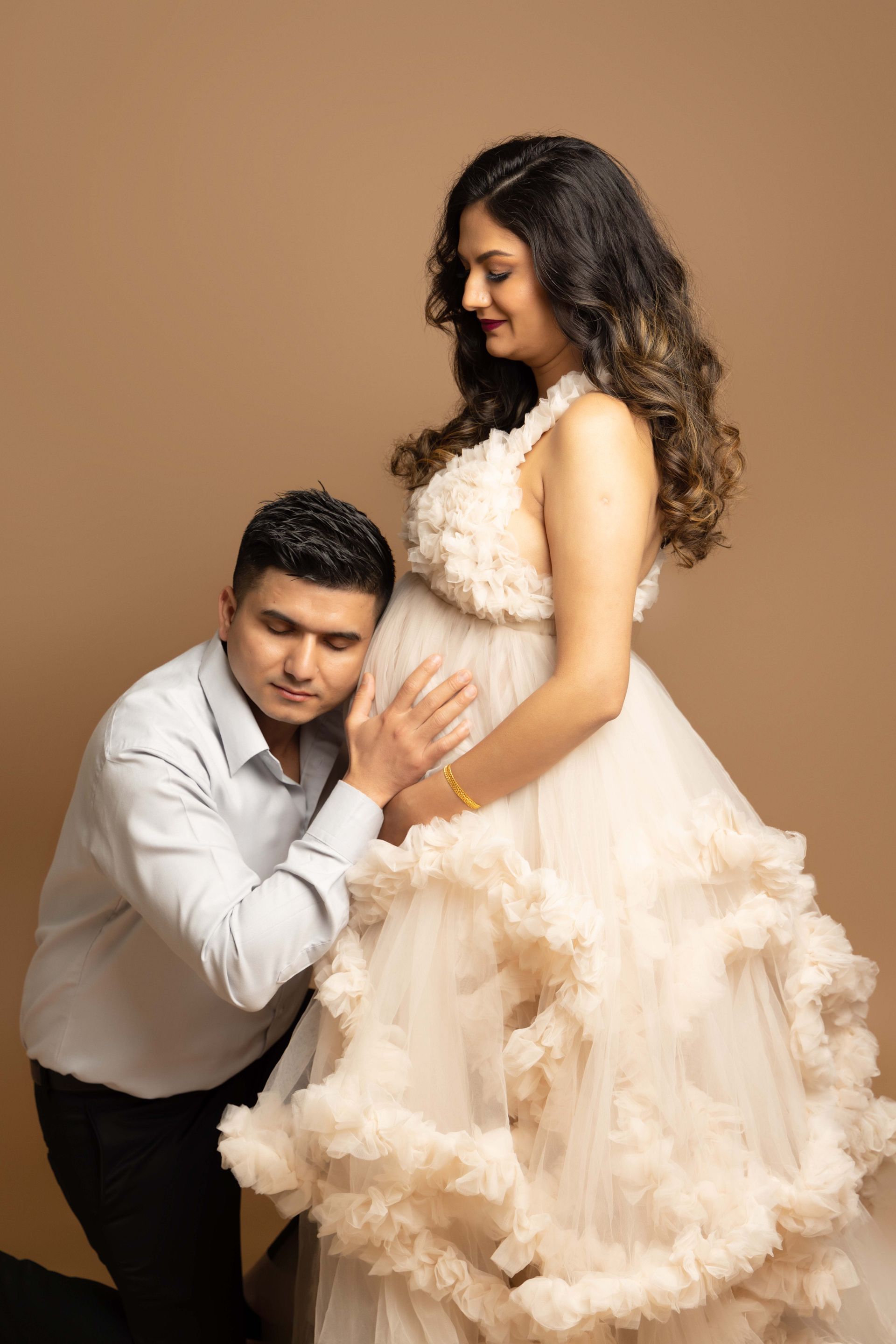 A man is kneeling down next to a pregnant woman in a white dress.