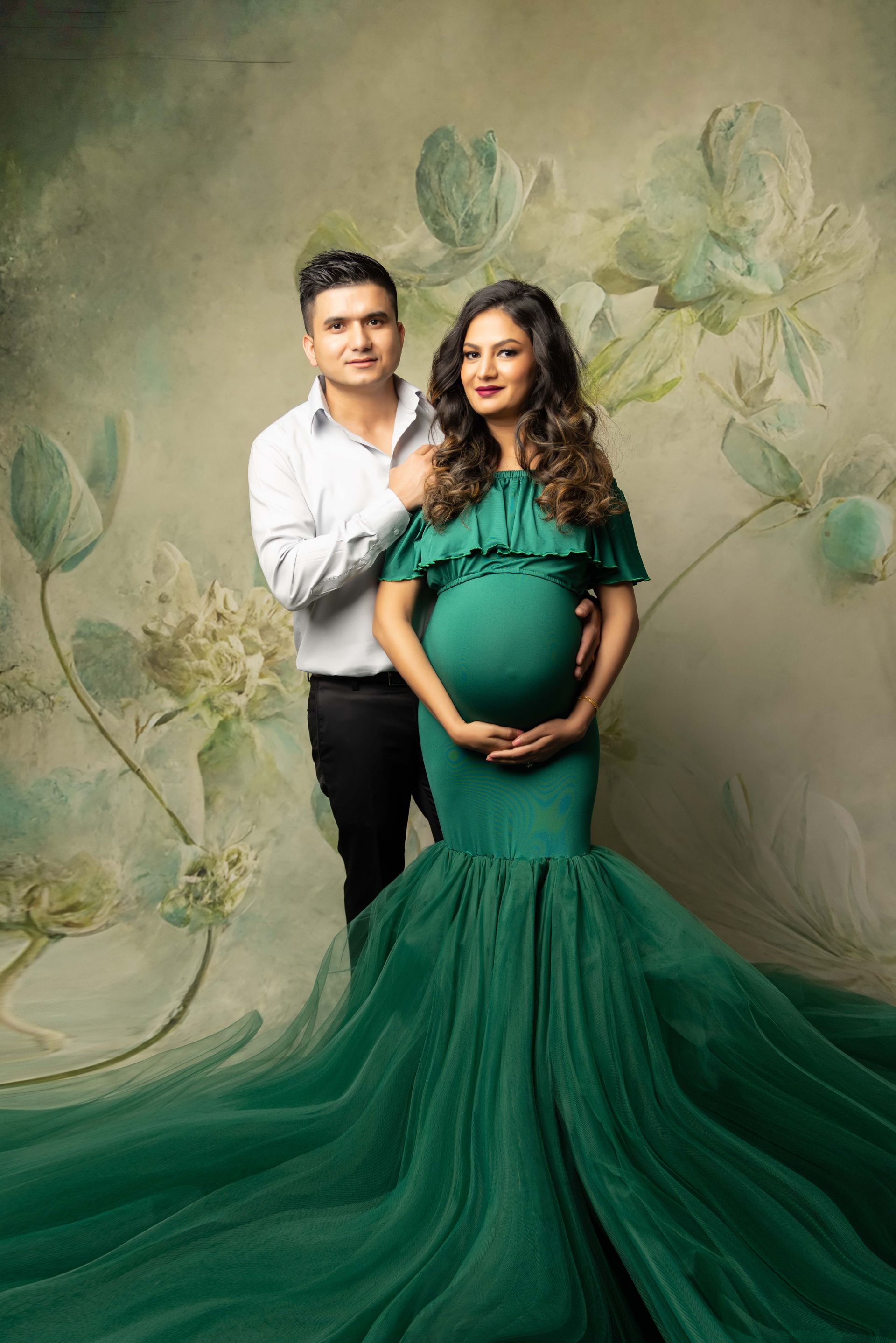 A man is standing next to a pregnant woman in a green dress.