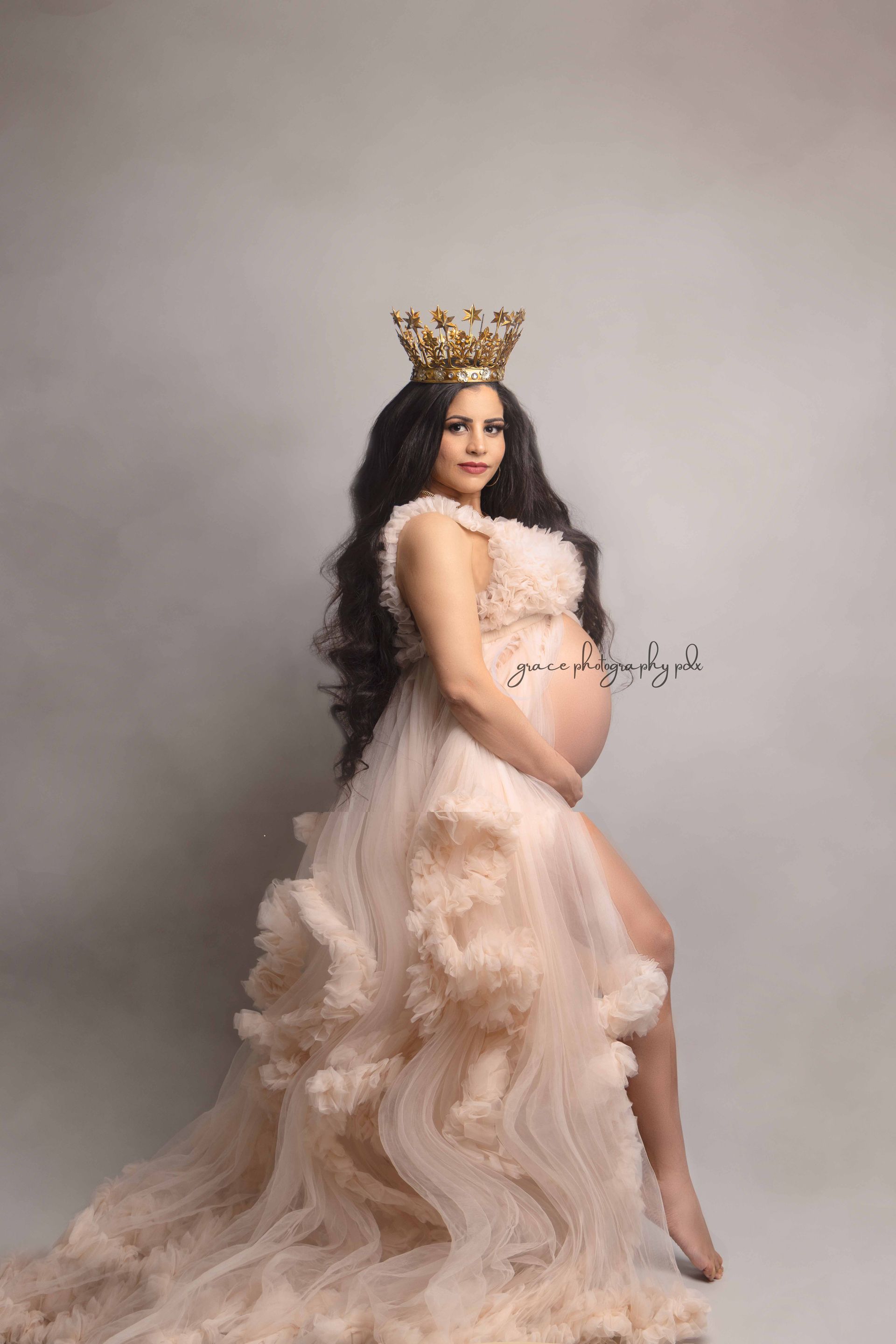 A pregnant woman is wearing a crown and a long dress.