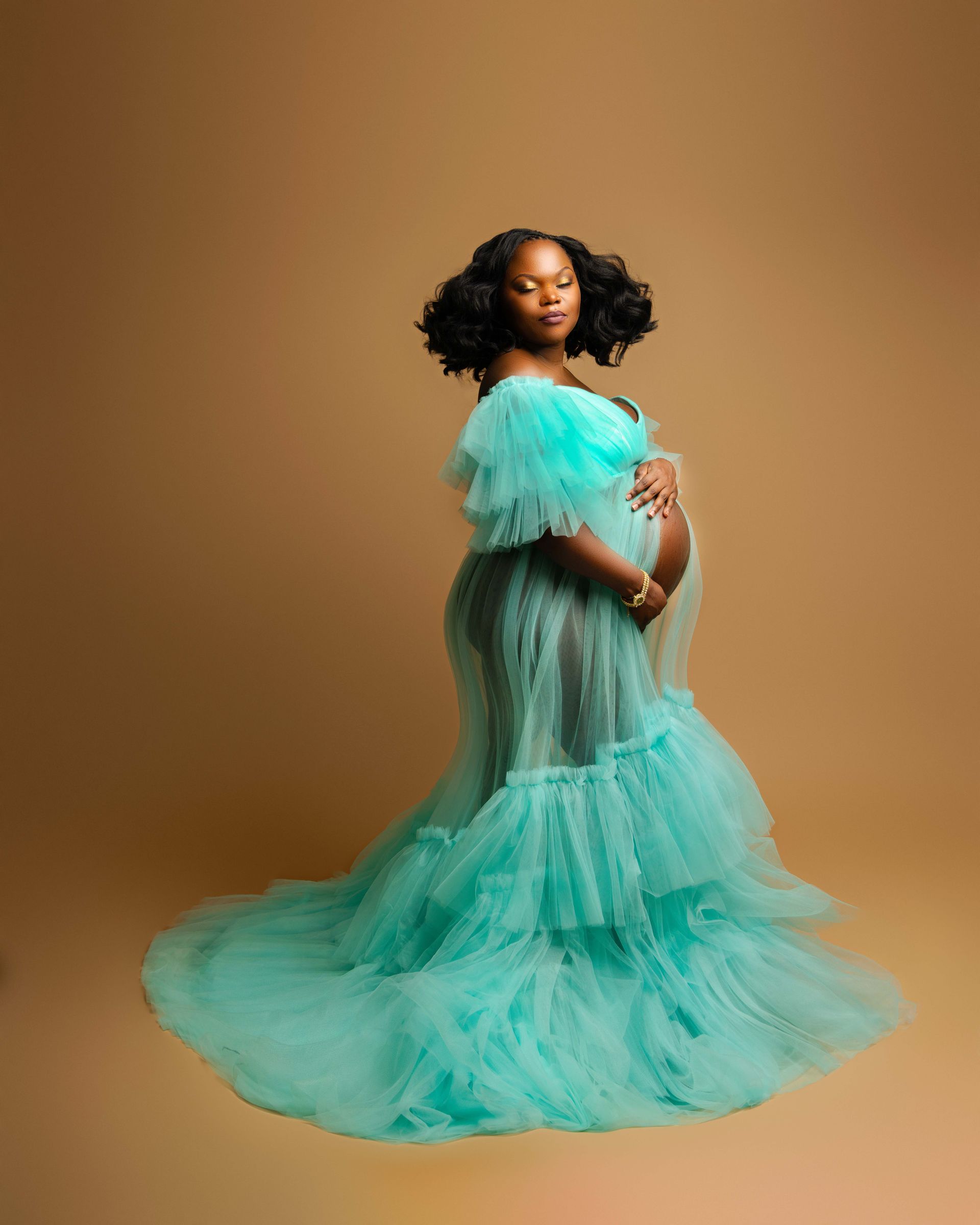 A pregnant woman is wearing a long green tulle dress and holding her belly.