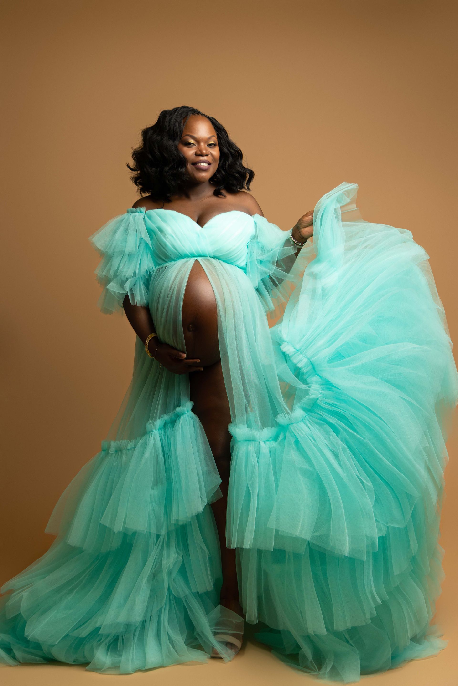 A pregnant woman is wearing a long green tulle dress.