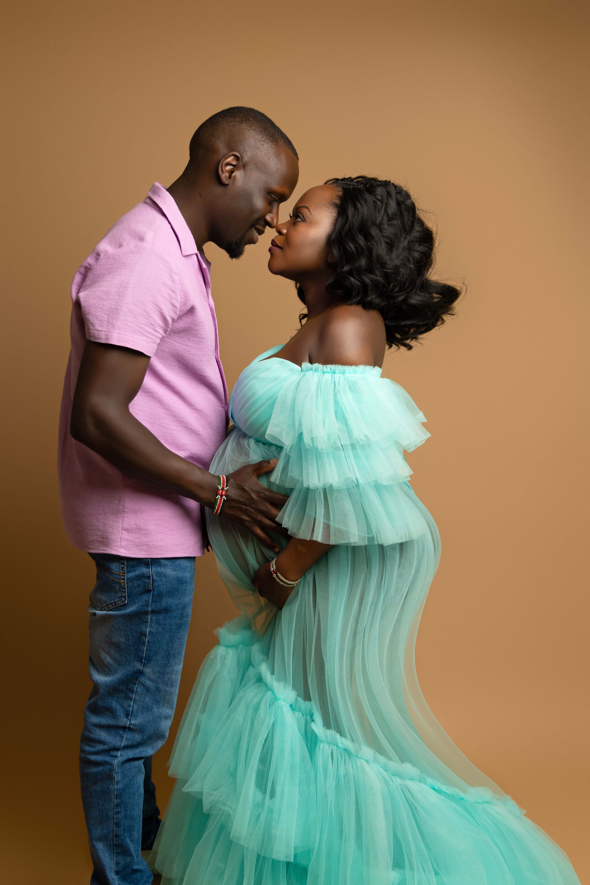 A pregnant woman in a green dress is standing next to a man in a pink shirt.