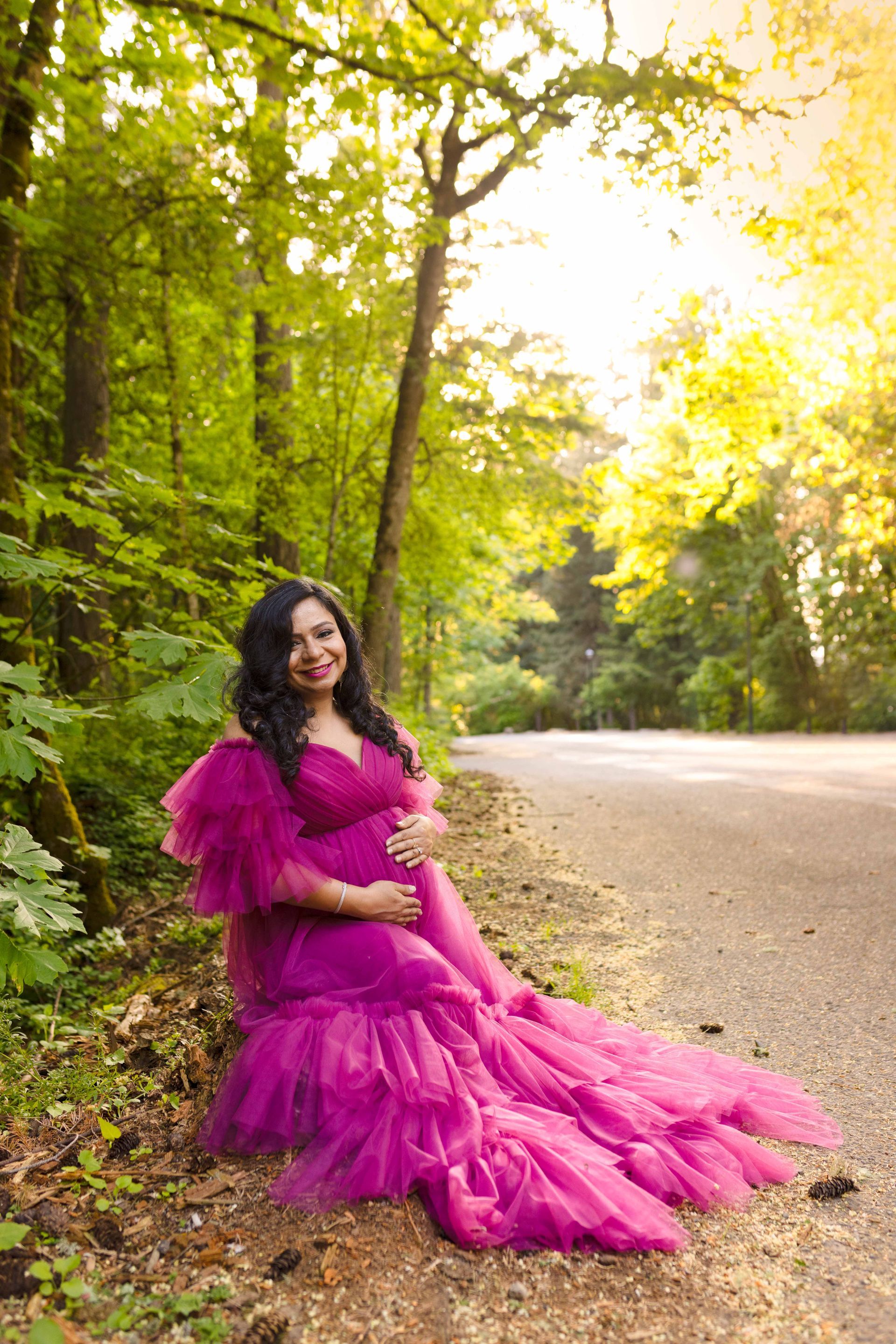 A pregnant woman in a pink dress is sitting on the side of a road.