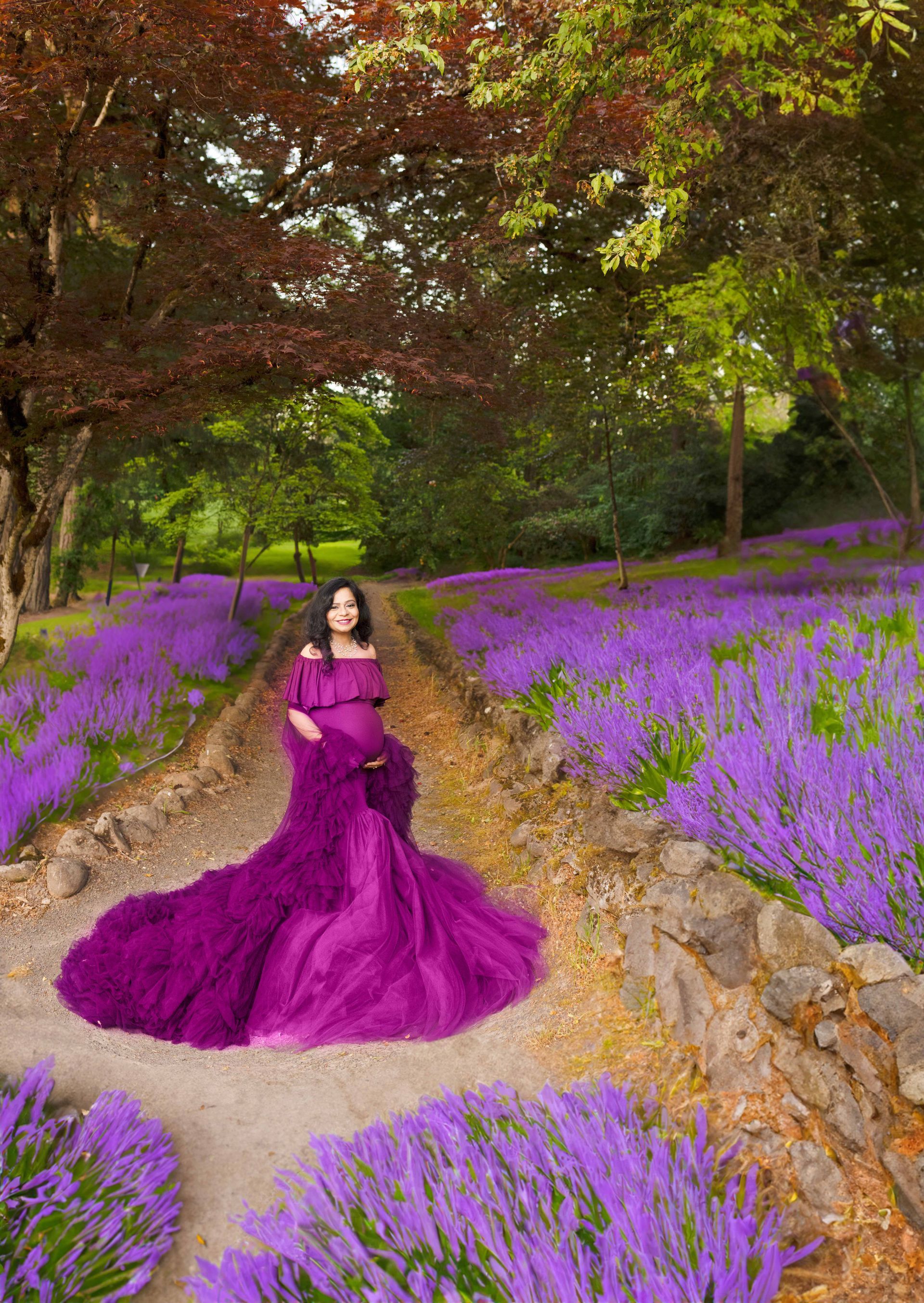 A pregnant woman in a purple dress is standing in a field of purple flowers.