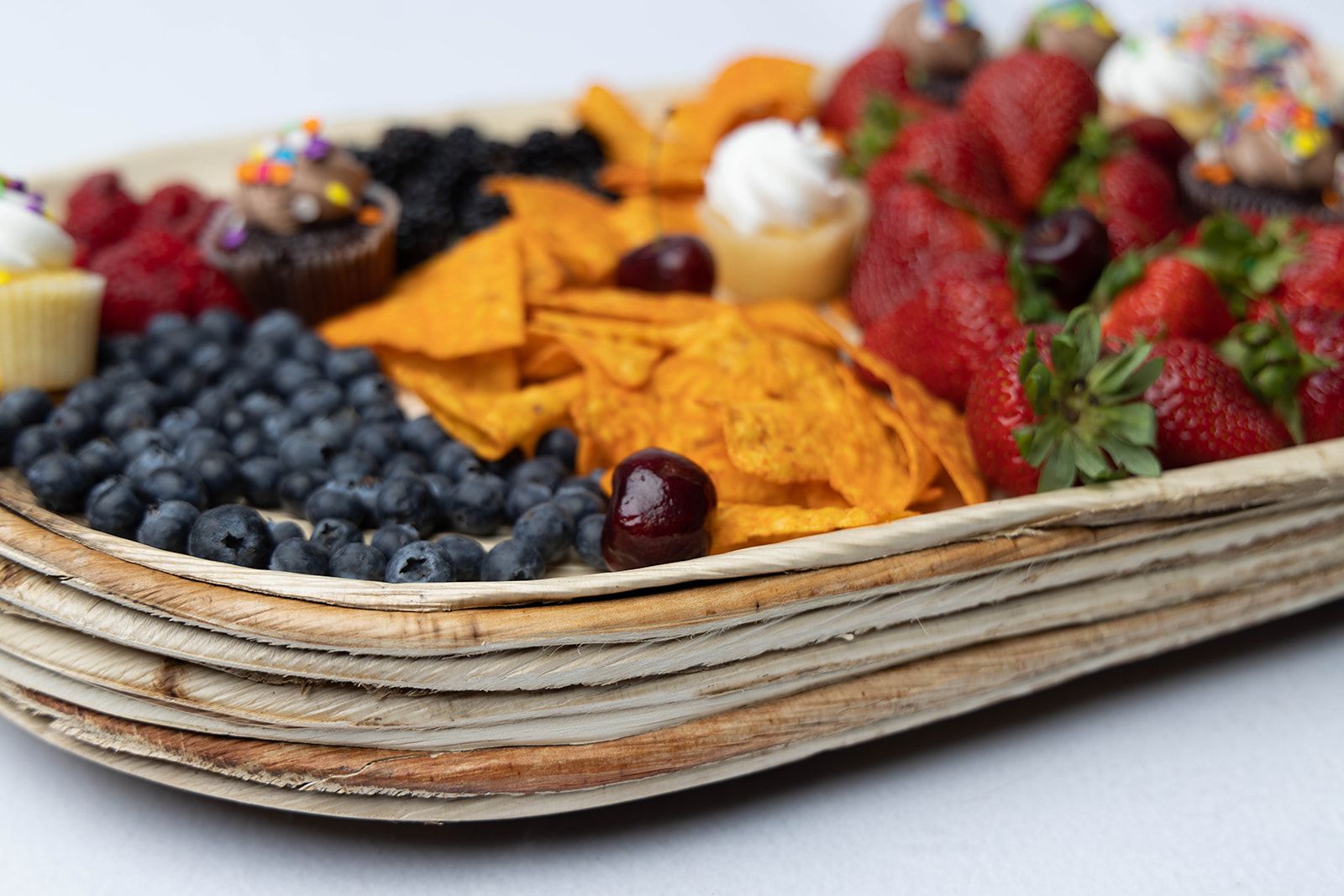 A wooden tray filled with fruit and chips on a table.