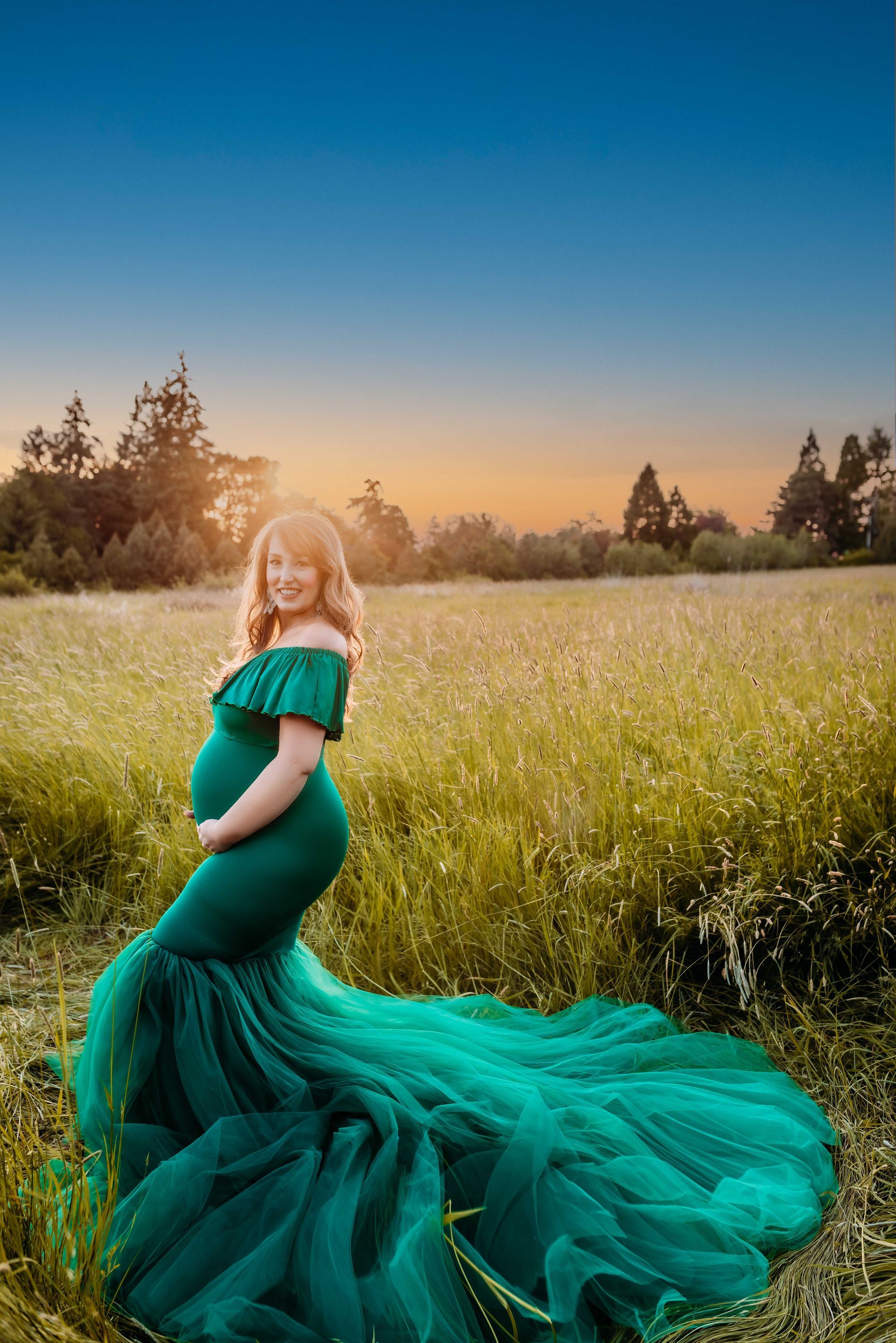 A pregnant woman in a green dress is standing in a field.