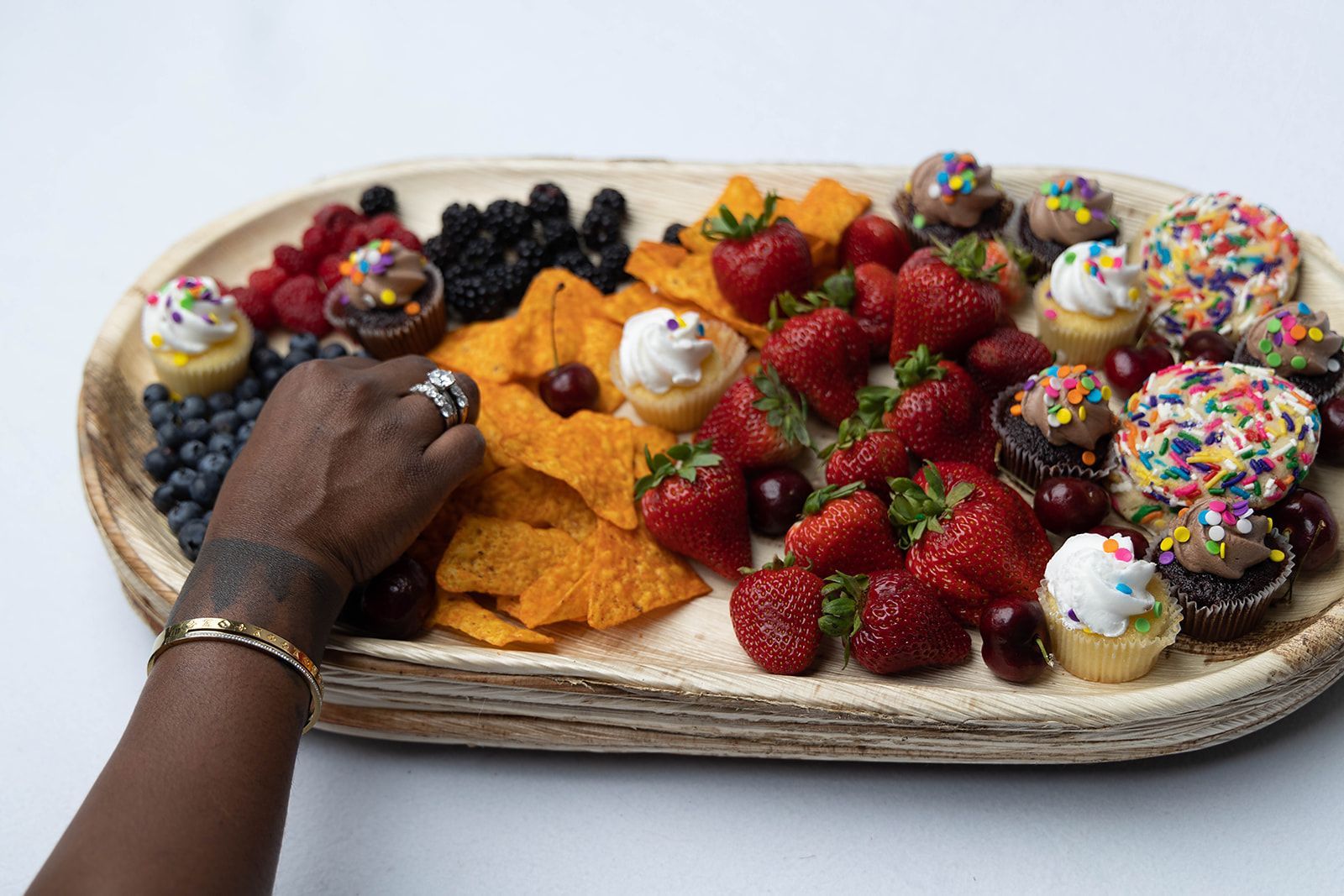 A person is reaching for a tray of fruit and desserts.