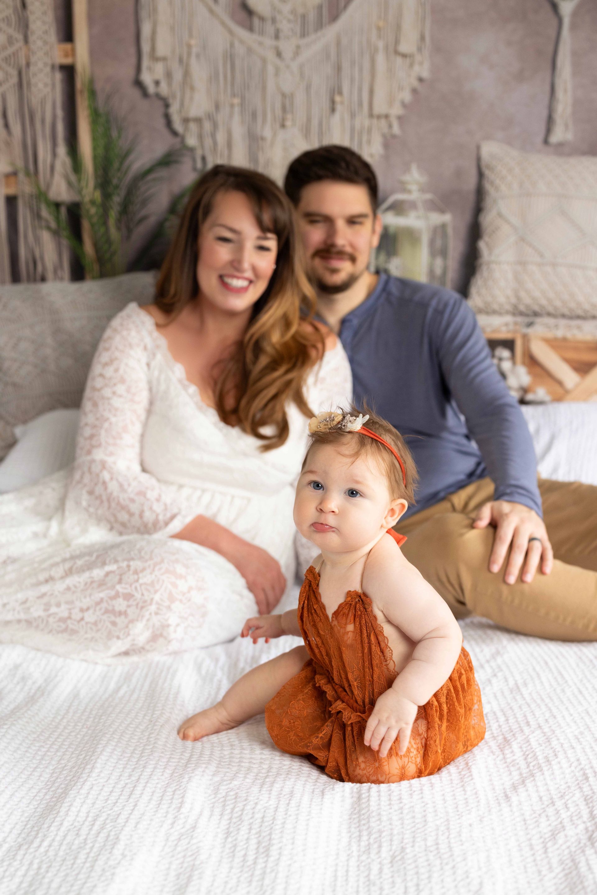 A family is sitting on a bed with a baby.