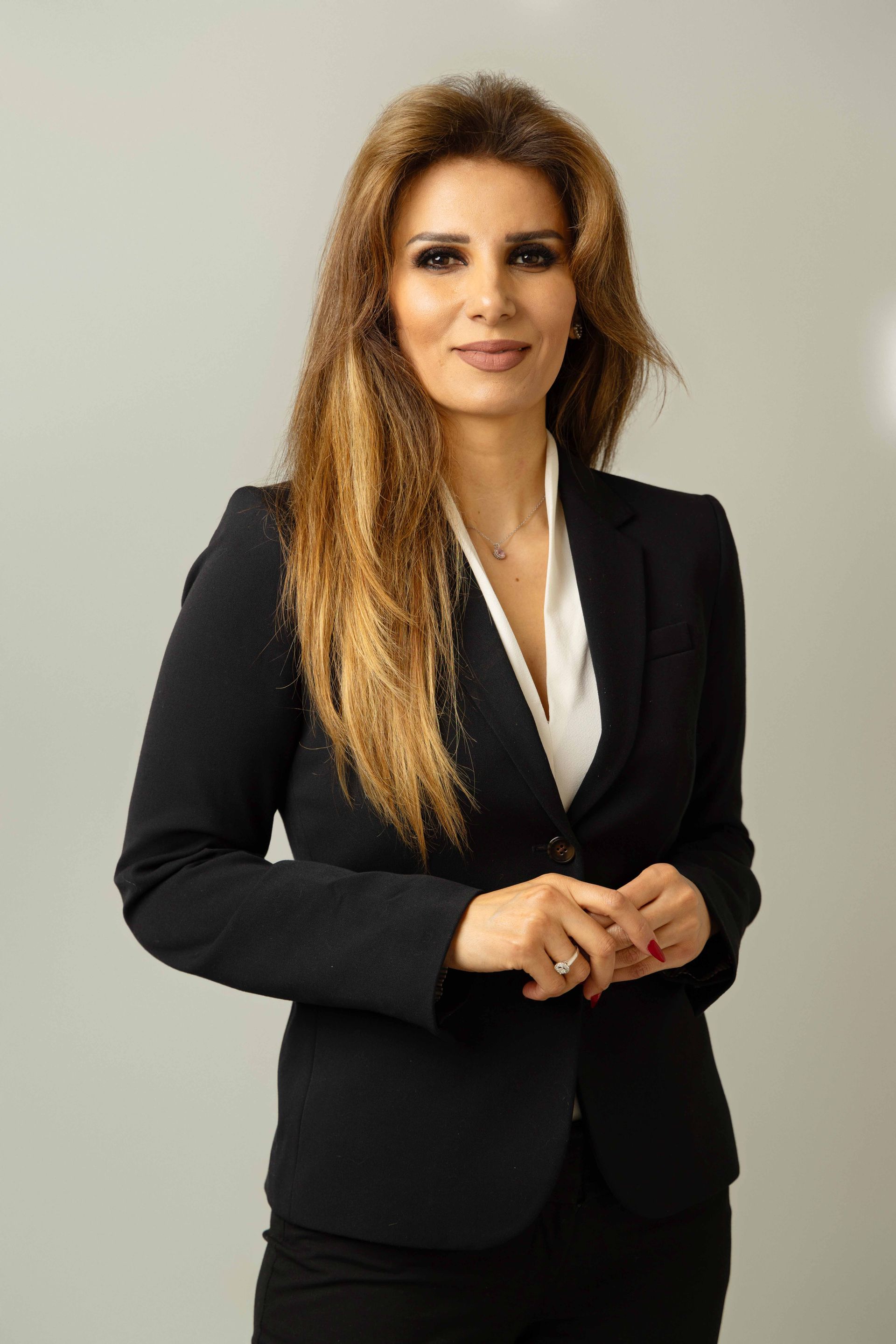 A woman in a black suit is standing in front of a white wall.