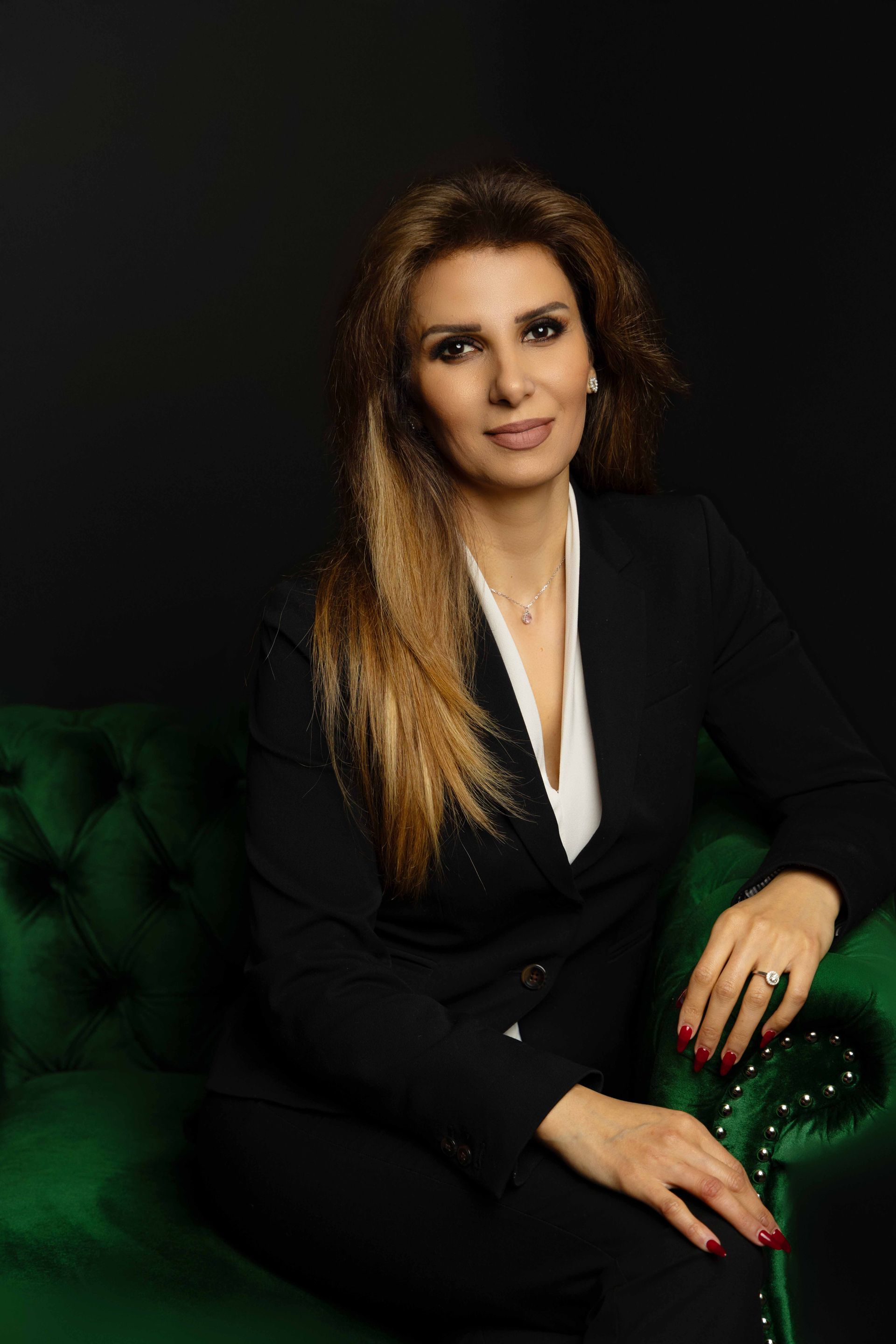 A woman in a black suit is sitting on a green couch.