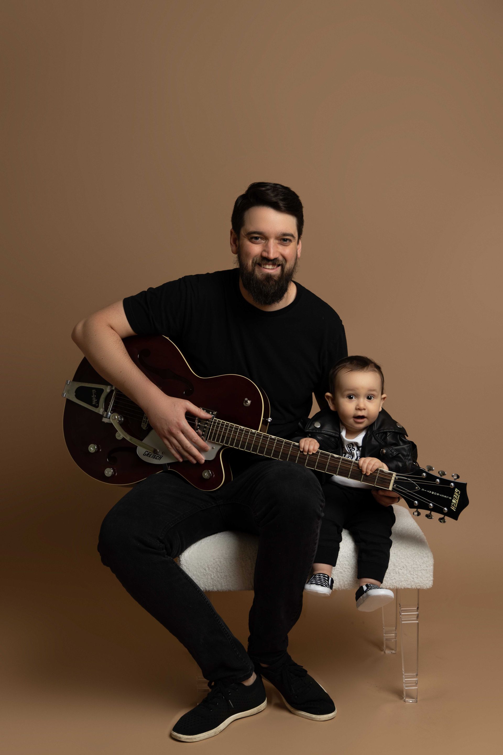 A man is sitting on a chair holding a guitar next to a baby.