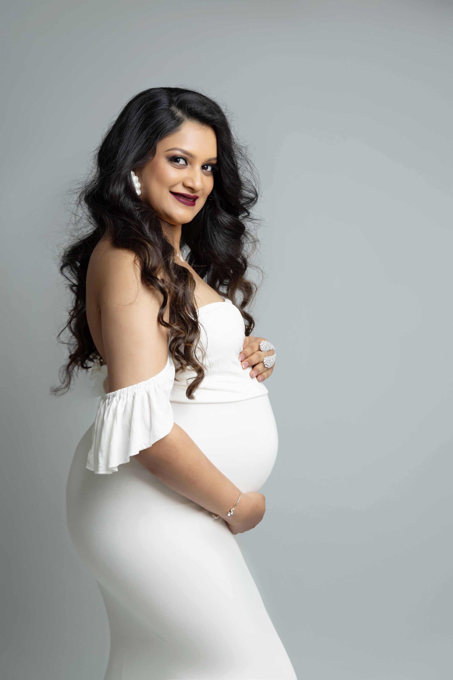 A pregnant woman in a white dress is holding her belly.