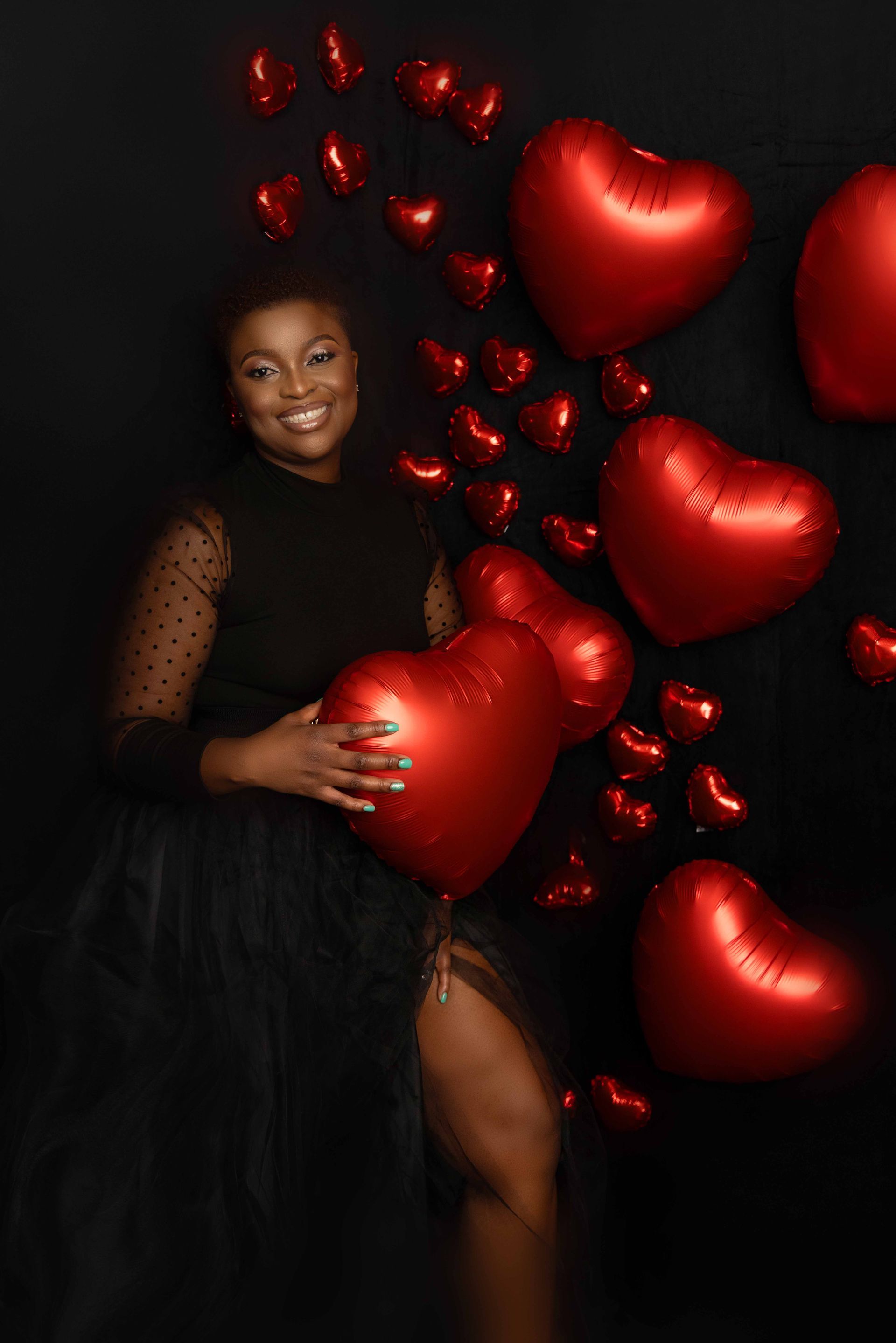 A woman in a black dress is holding a red heart shaped balloon.