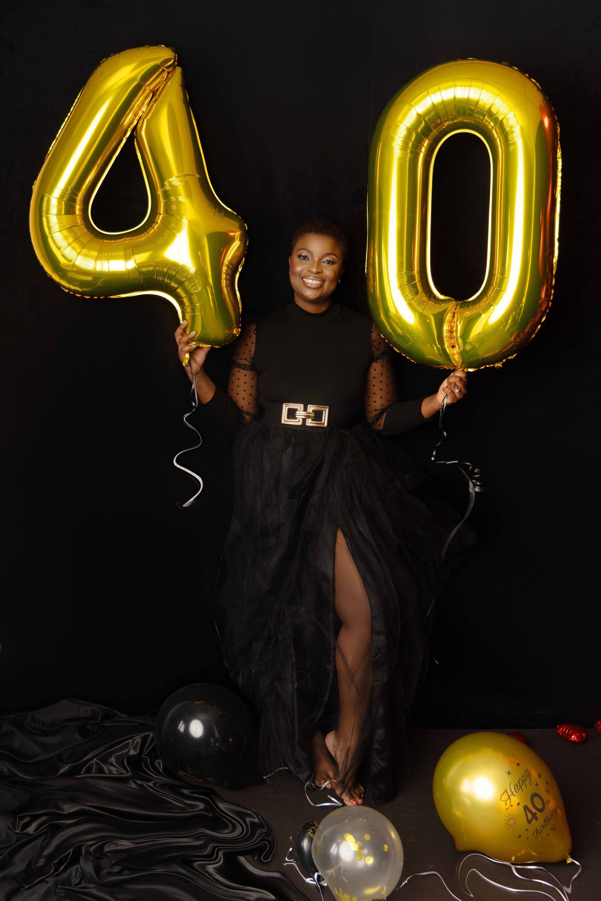 A woman is holding balloons in the shape of the number 40.