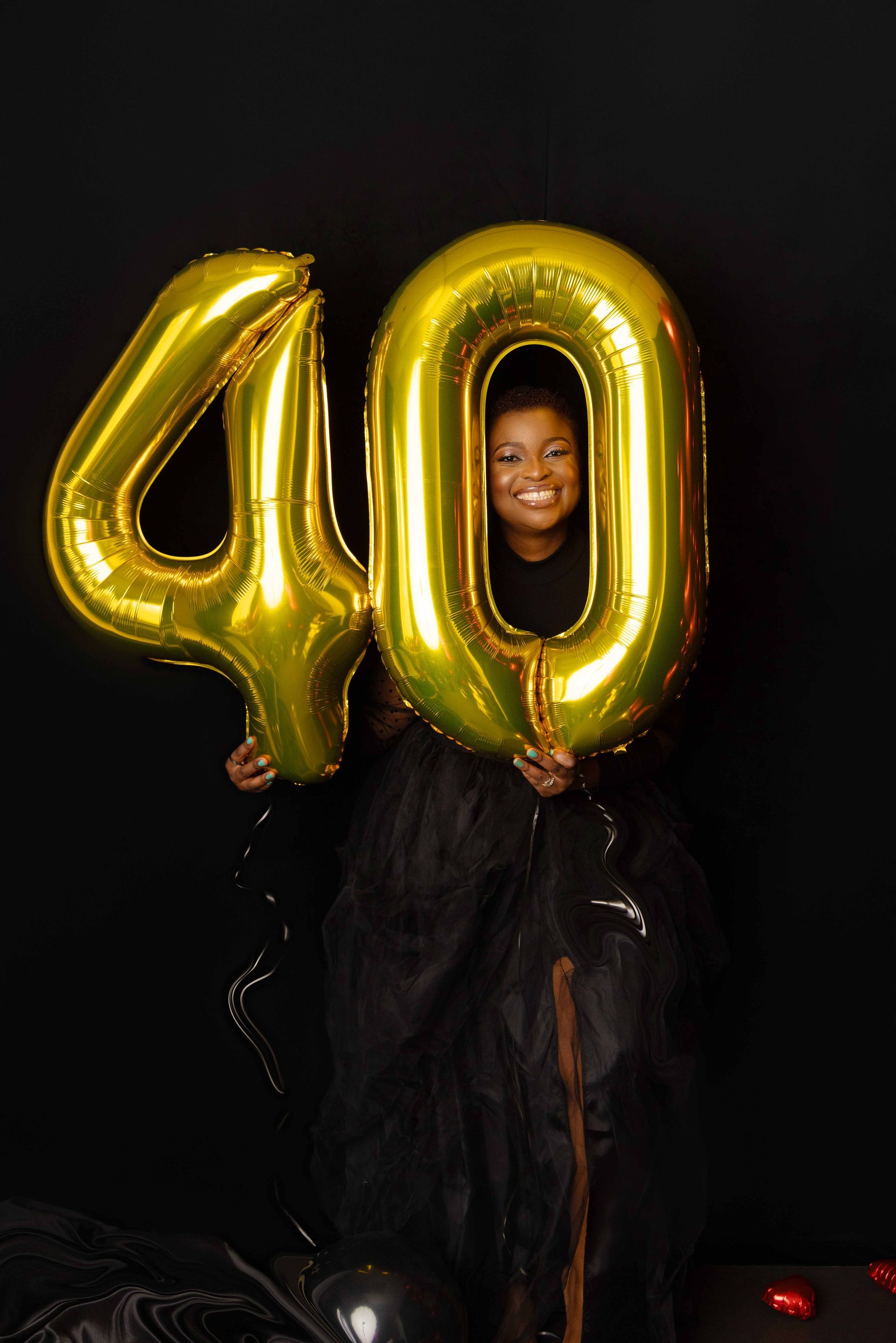 A woman in a black dress is holding a gold balloon in the shape of the number 40.