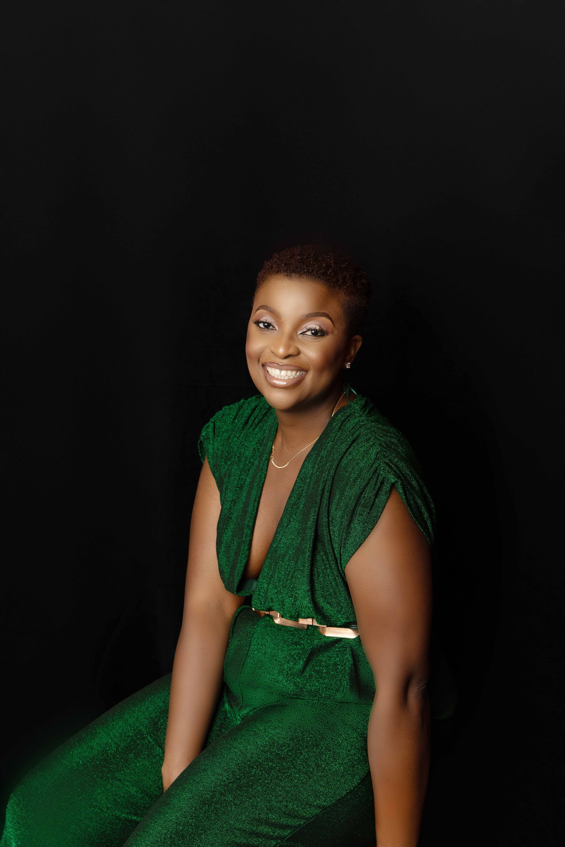 A woman in a green dress is sitting in front of a black background.