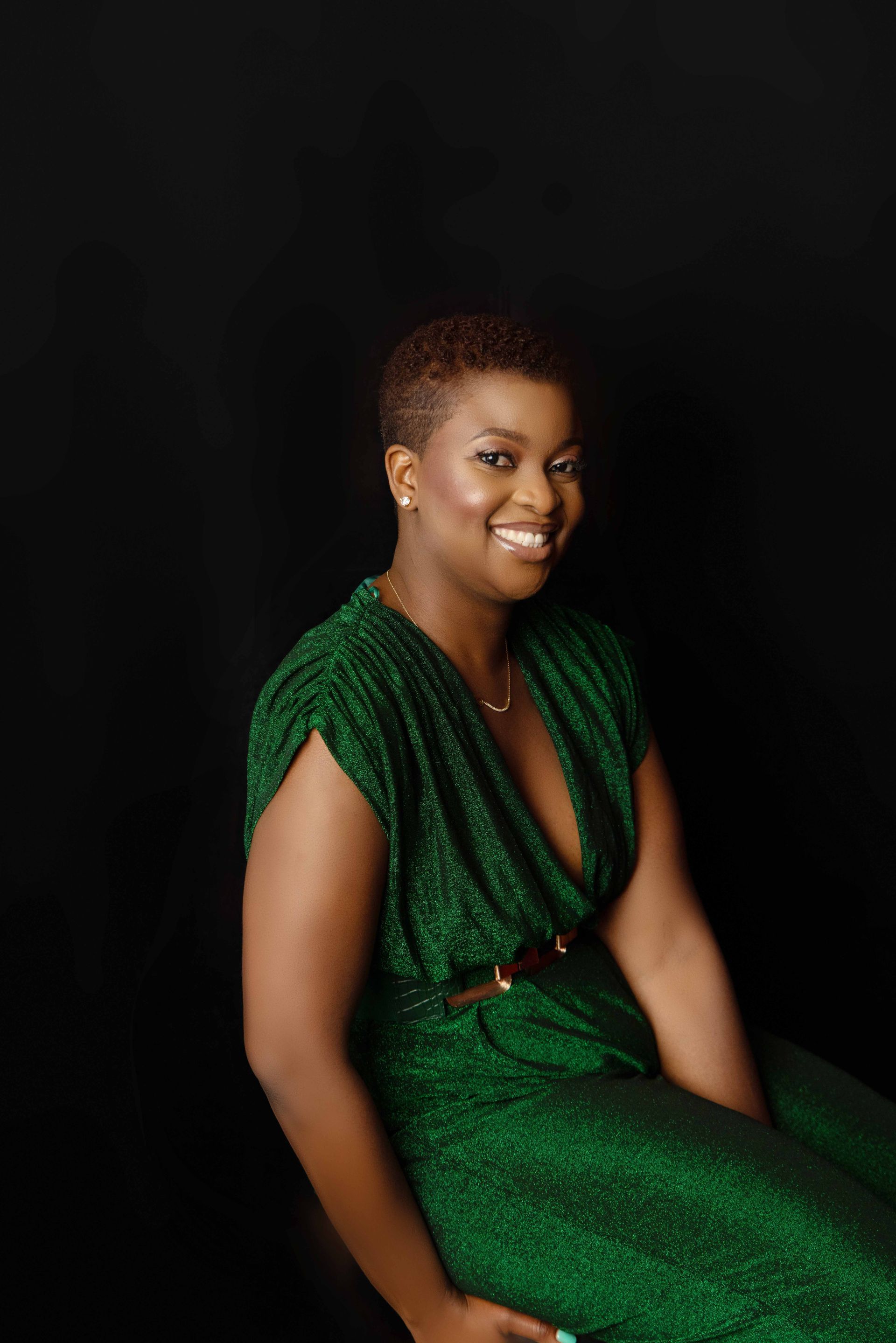 A woman in a green dress is sitting in front of a black background and smiling.