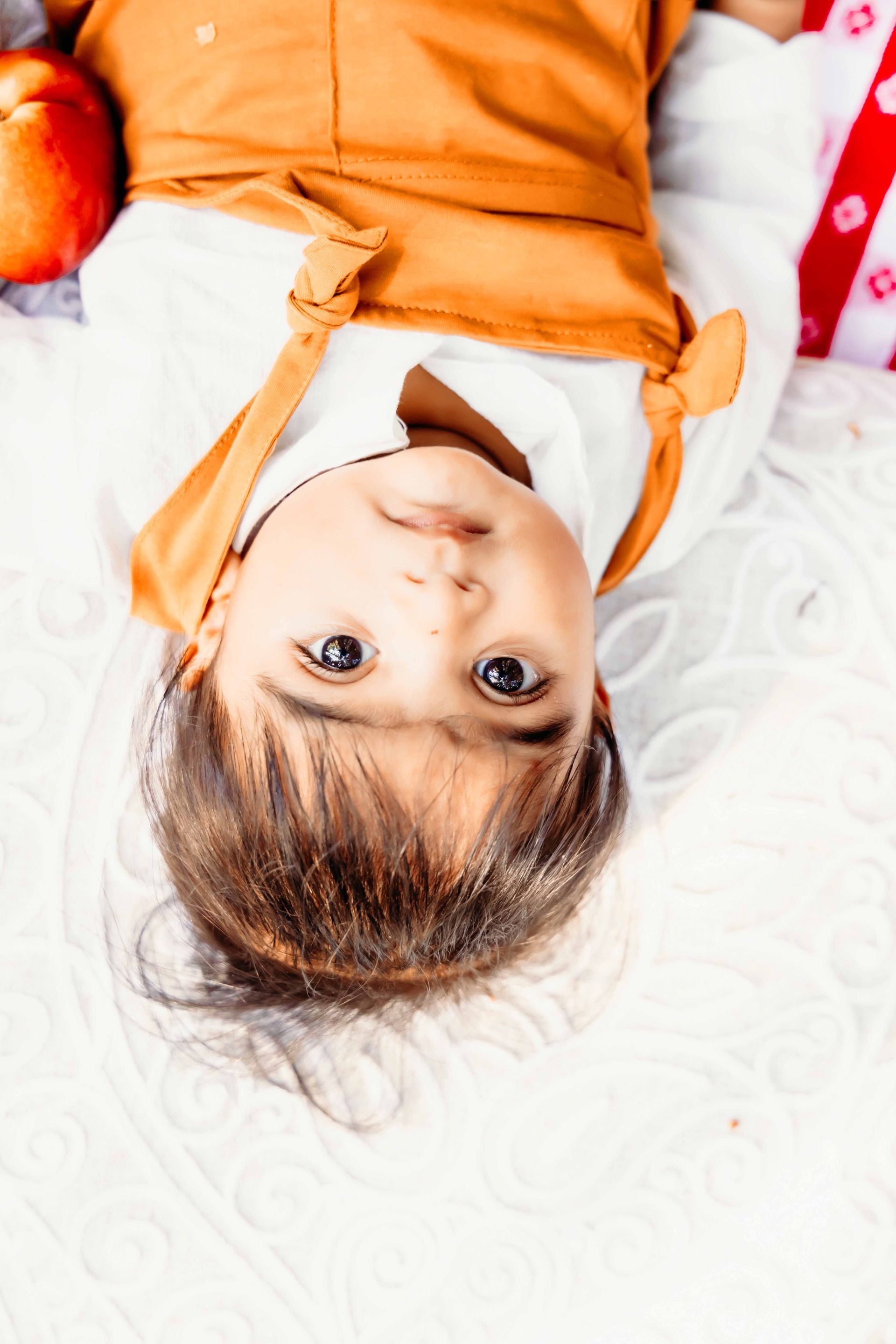 A little girl is laying upside down on a white blanket.