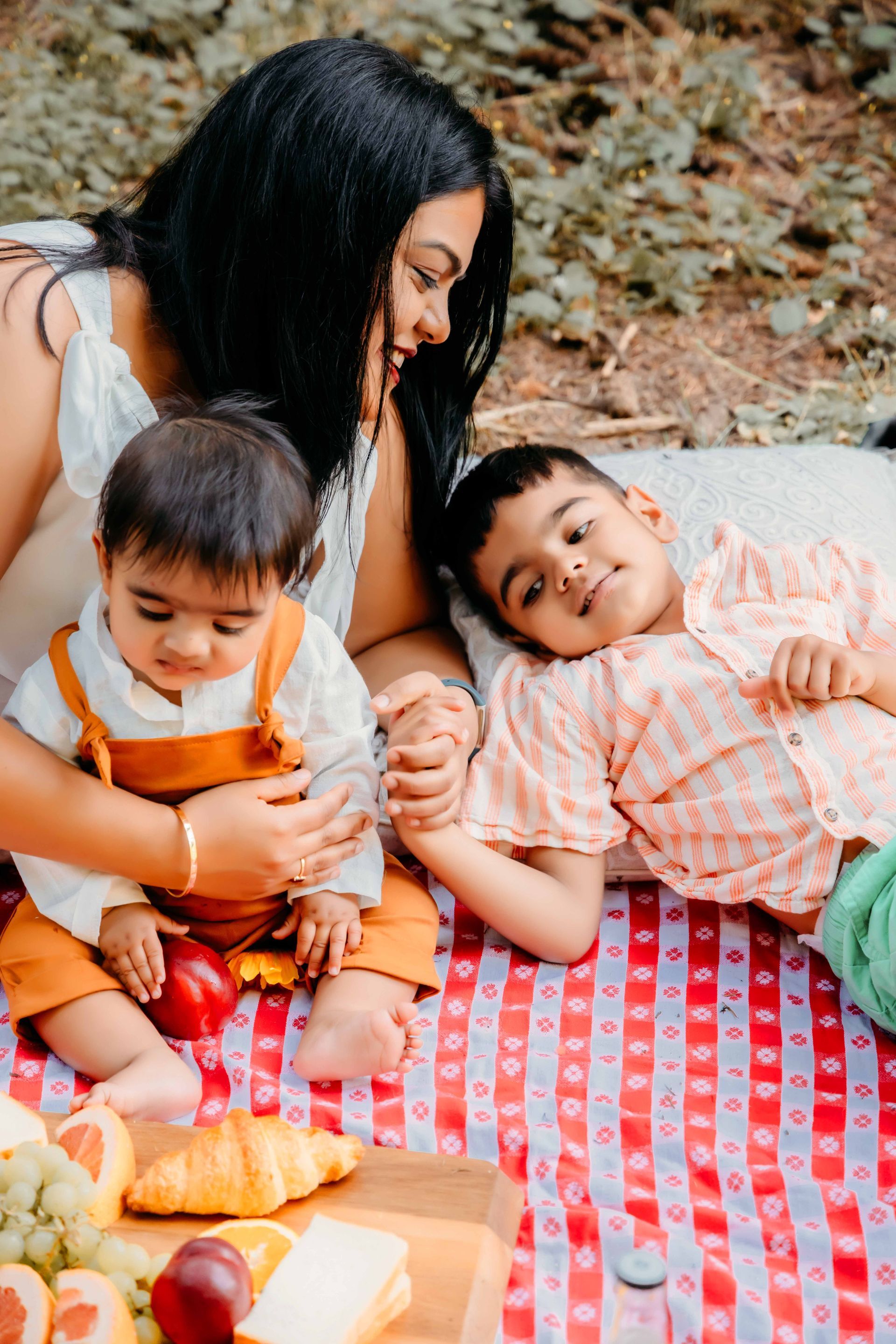 A woman is laying on a picnic blanket with two children.