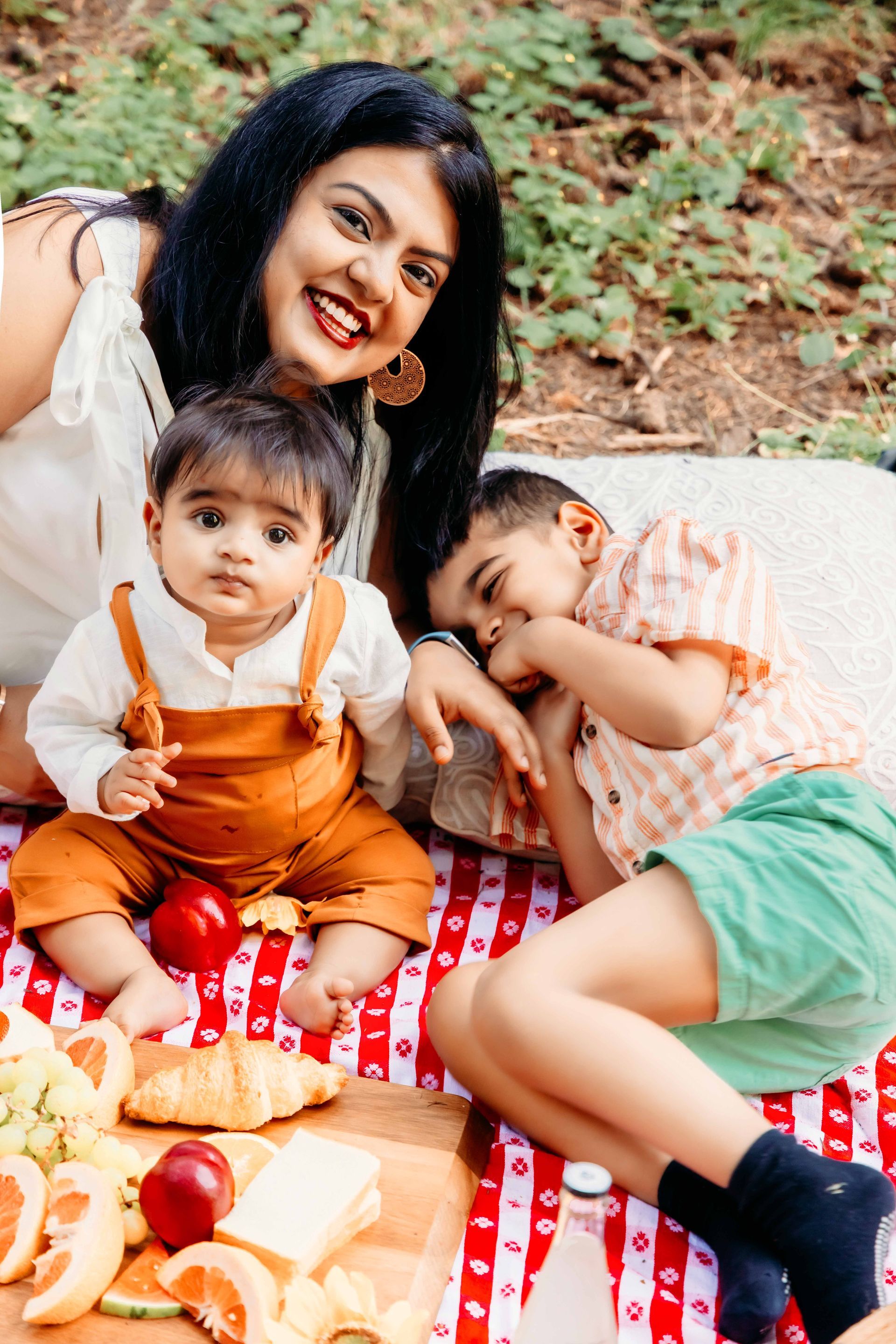 A woman is sitting on a picnic blanket with two children.
