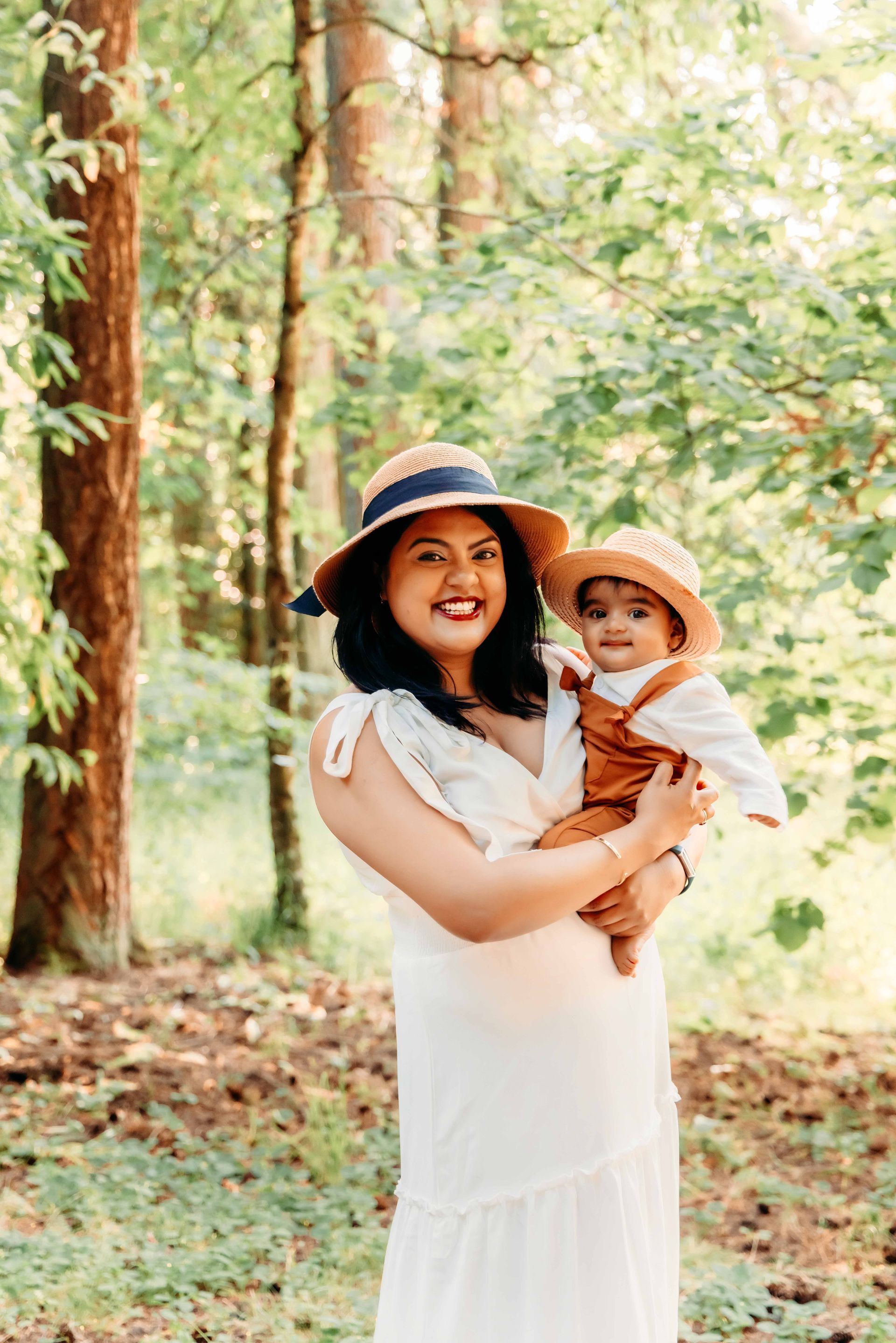 A pregnant woman is holding a baby in her arms in the woods.