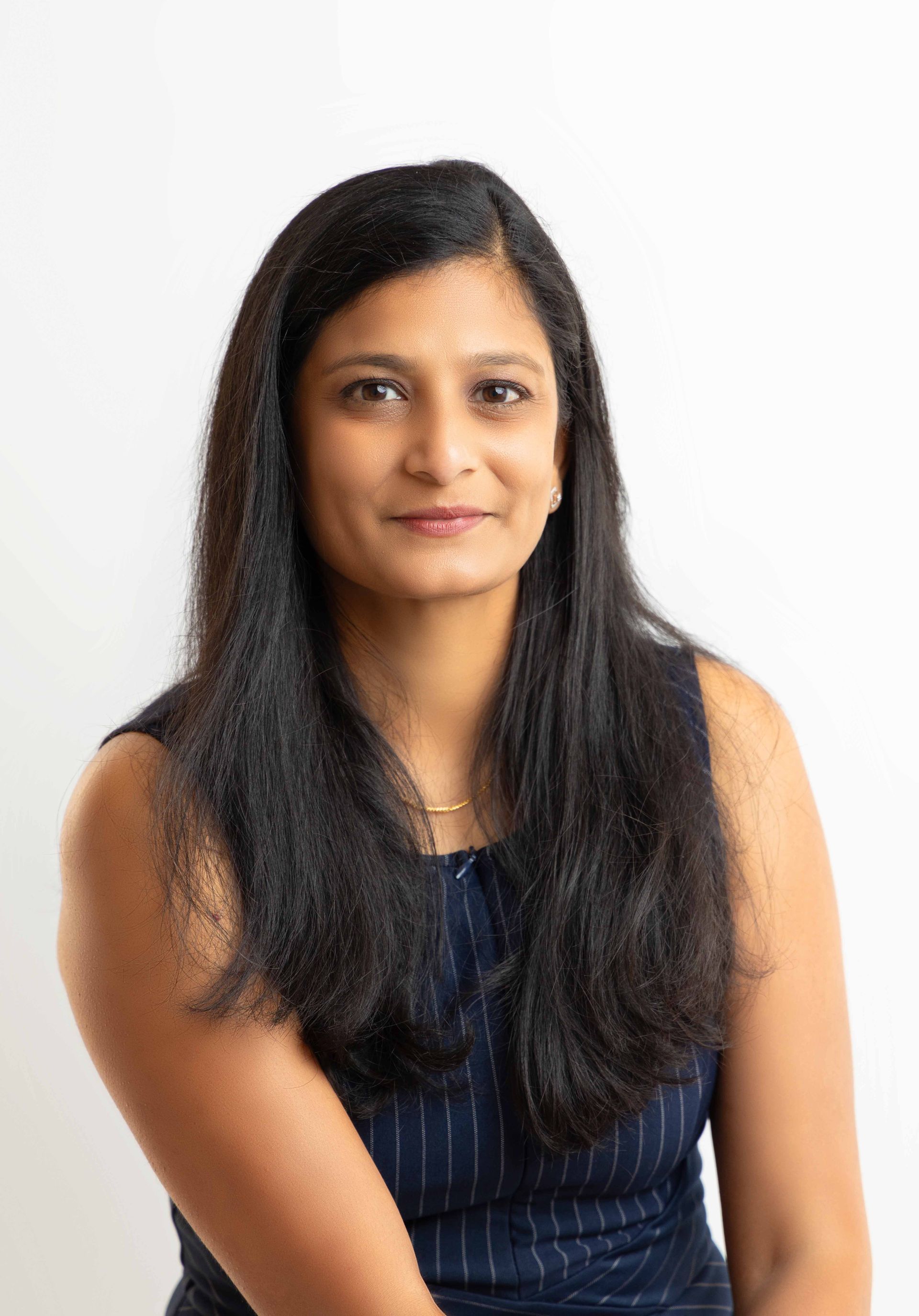 A woman with long black hair is sitting in front of a white background.