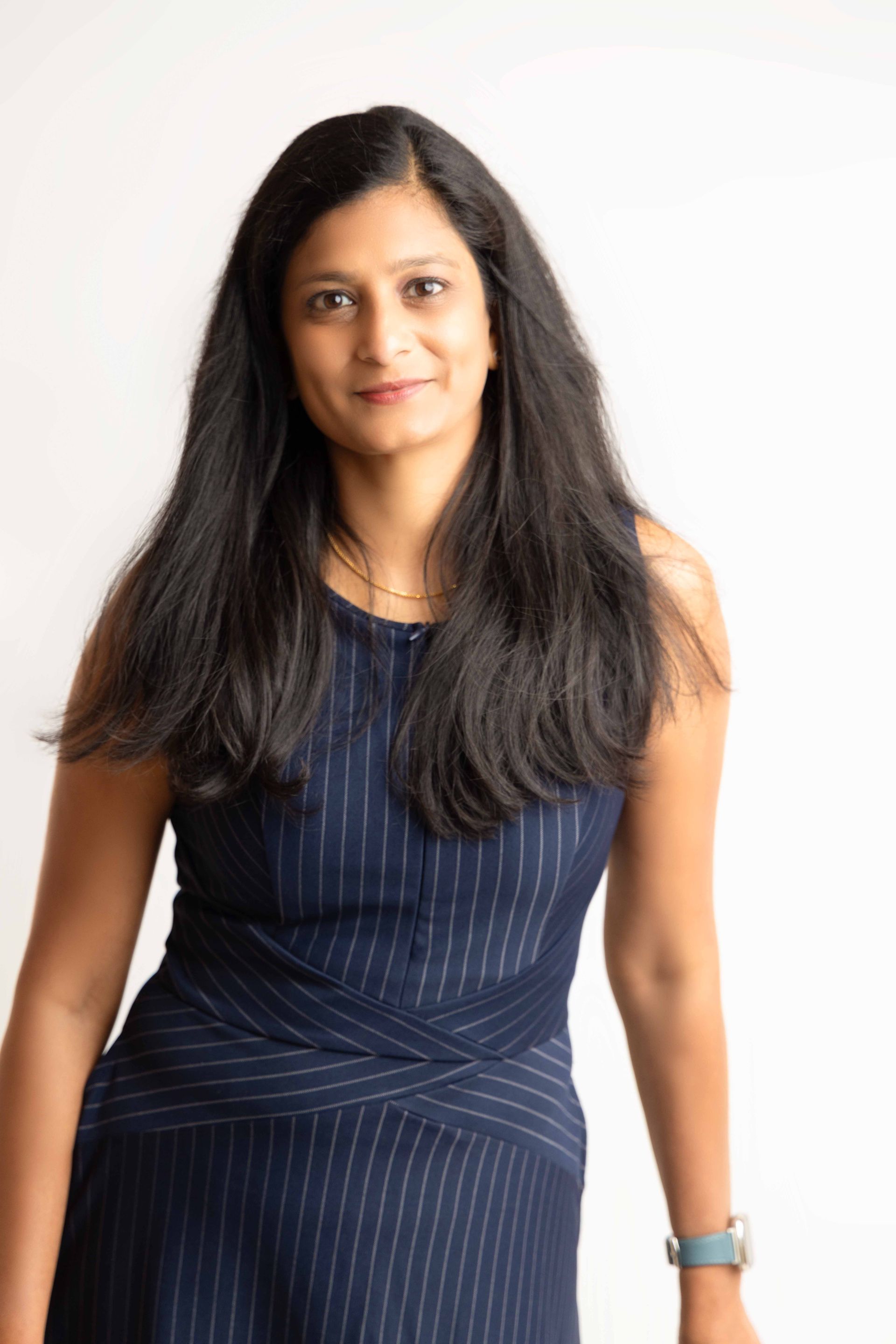 A woman in a blue dress is standing in front of a white background.