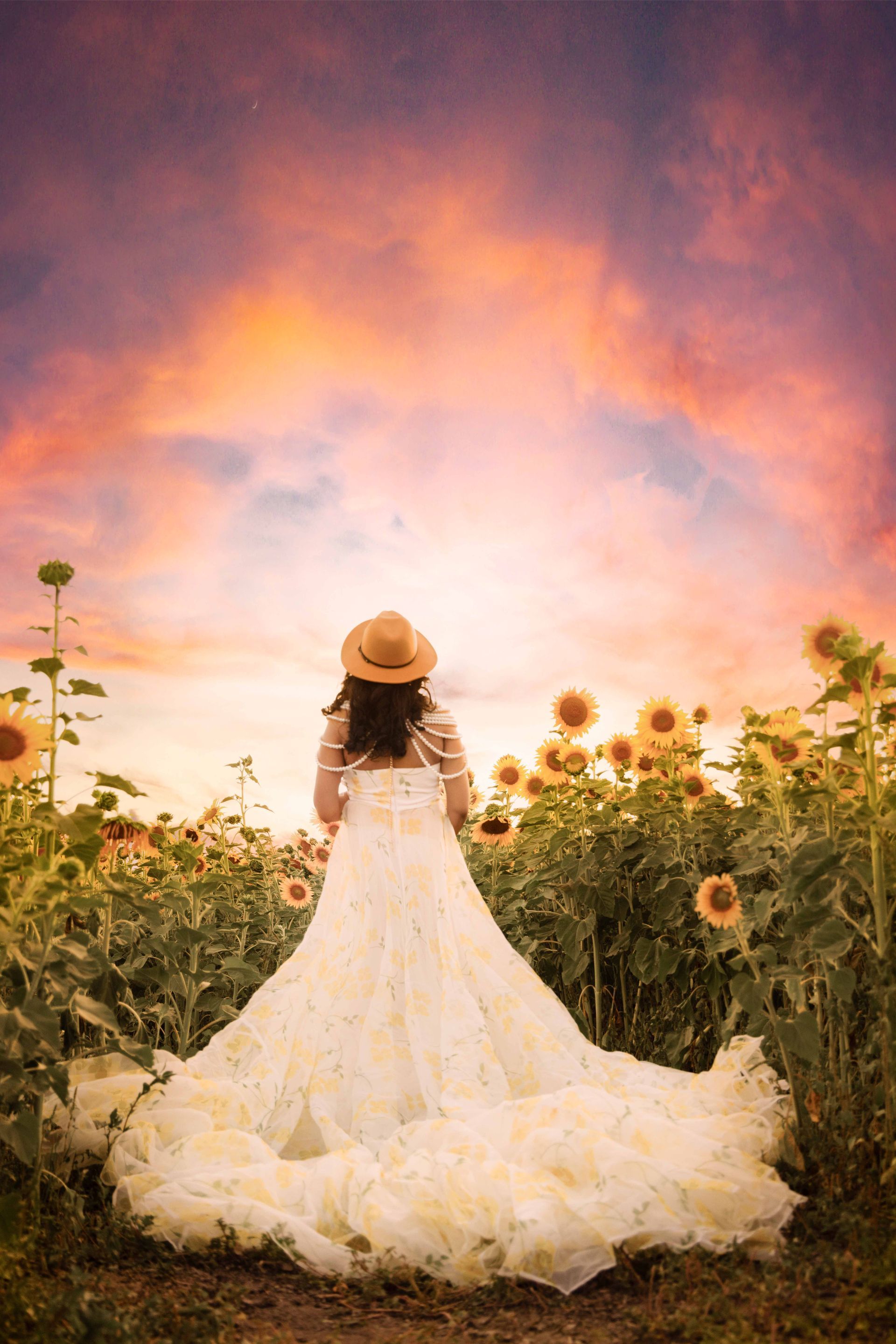 A woman in a wedding dress and hat is standing in a field of sunflowers.