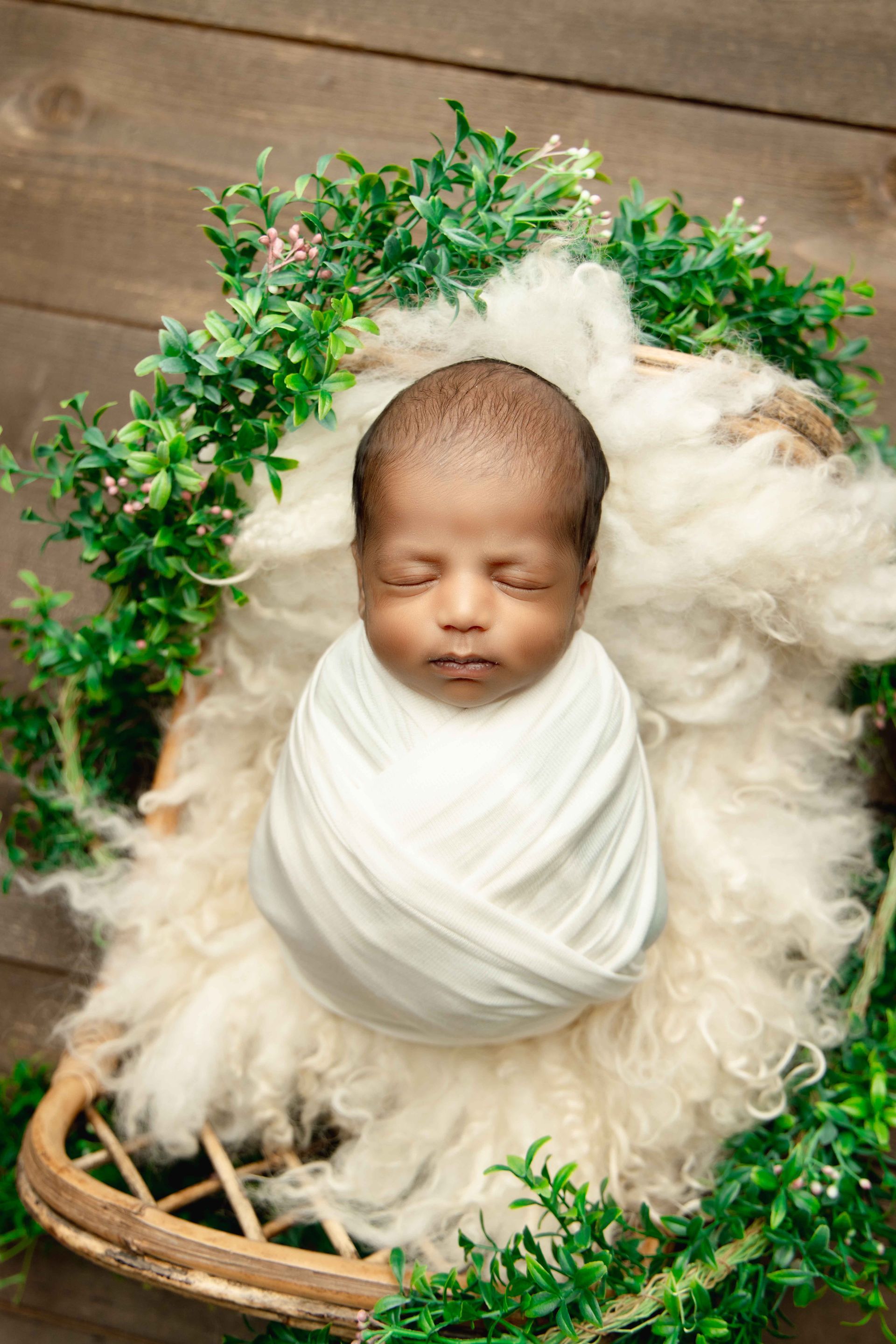 A newborn baby wrapped in a white blanket is sleeping in a basket.