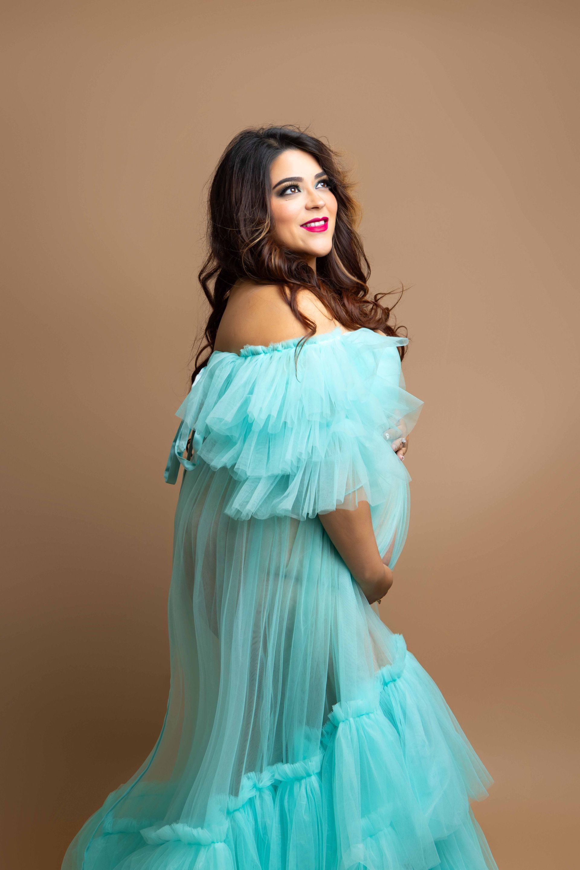 A pregnant woman is wearing a blue tulle dress and holding her belly.